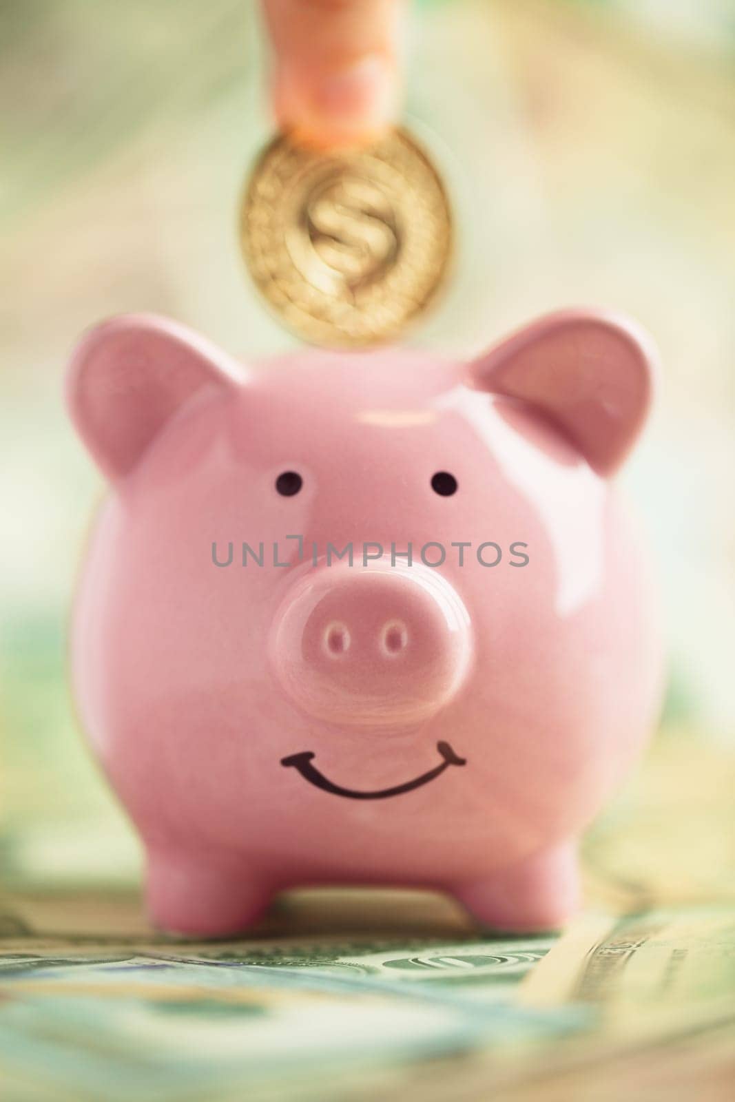 Depositing gold coin in smiling pink Piggybank on piles of money. Saving money concept.
