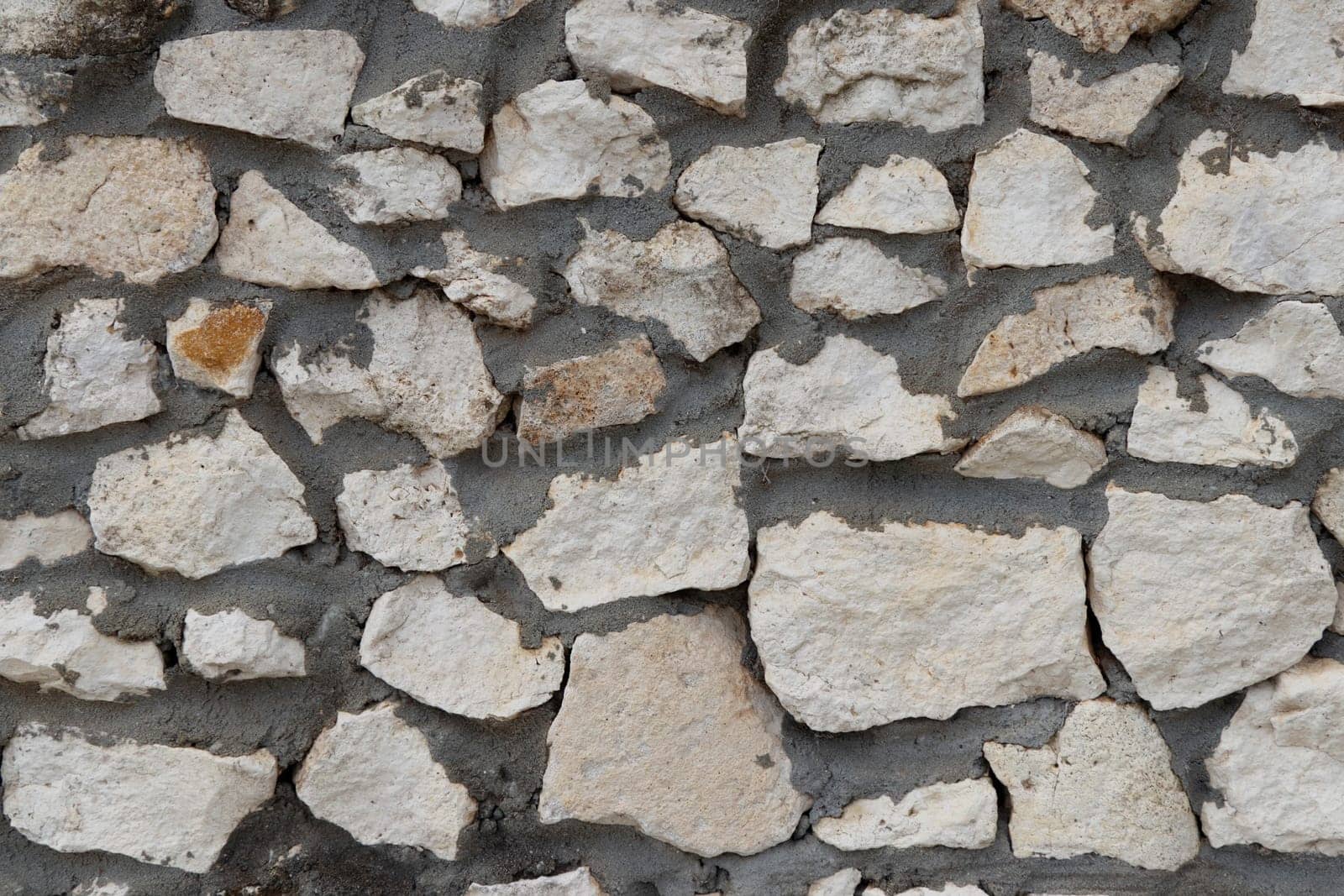 Natural off-white rough rock stone mixed with dark gray cement wall background surface close-up in the day. Close-up background of rough light gray stone and dark gray cement wall outside in the day.