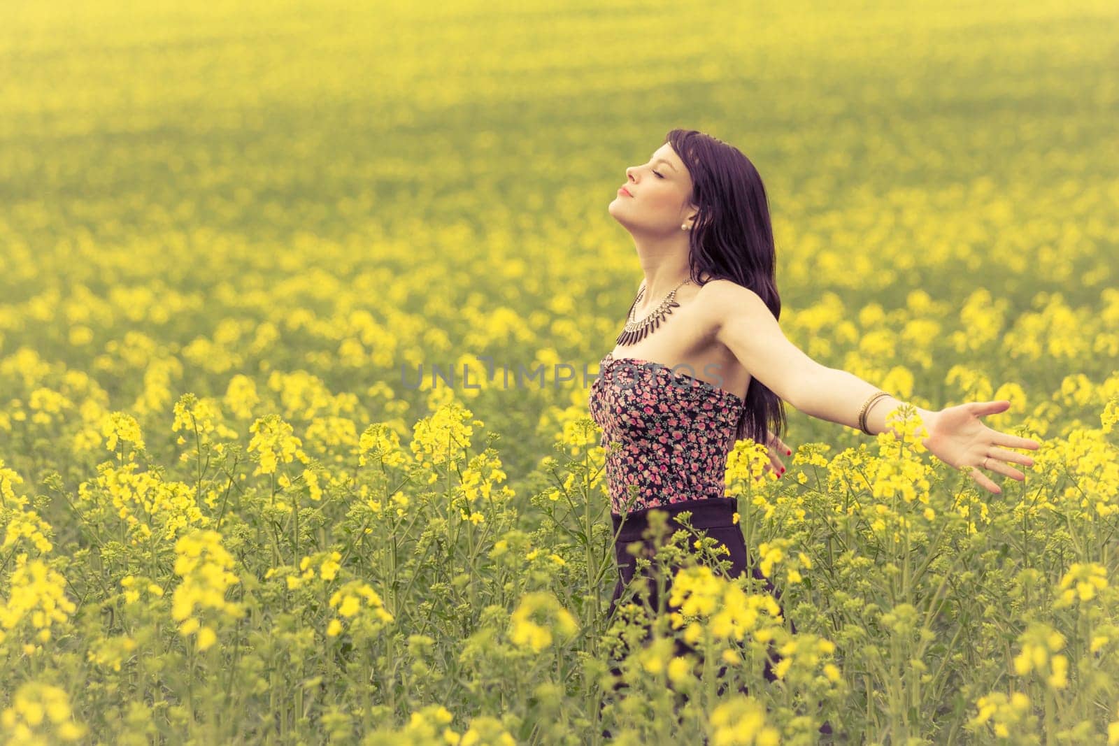 Attractive young beauty girl enjoying the warm sunny sun in nature rapeseed field takes time feeling sustainability and contemplation.