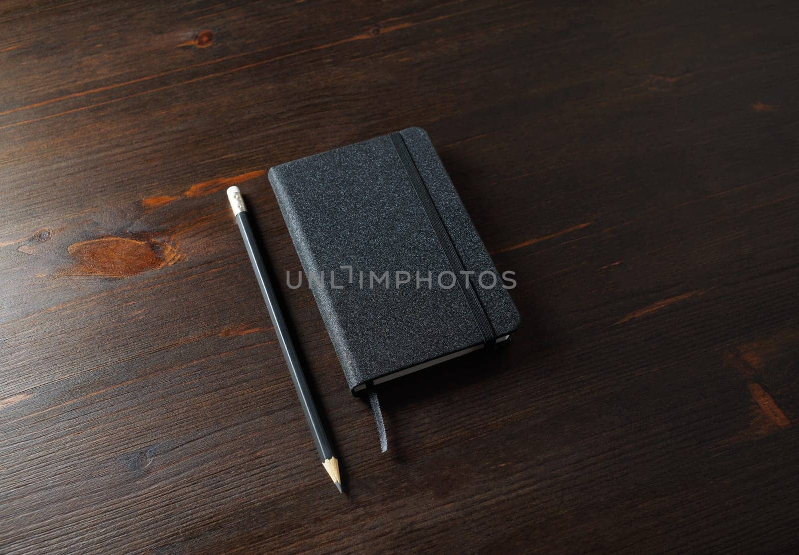 Photo of black notepad and pencil on wood table background.