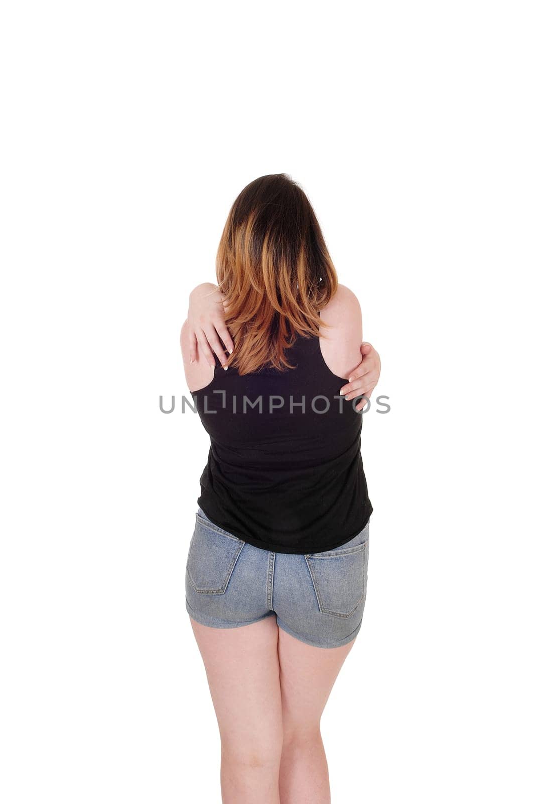 A lovely woman standing from the back in jeans shorts and hugging.herself with her arms on her shoulders, isolated for white background.