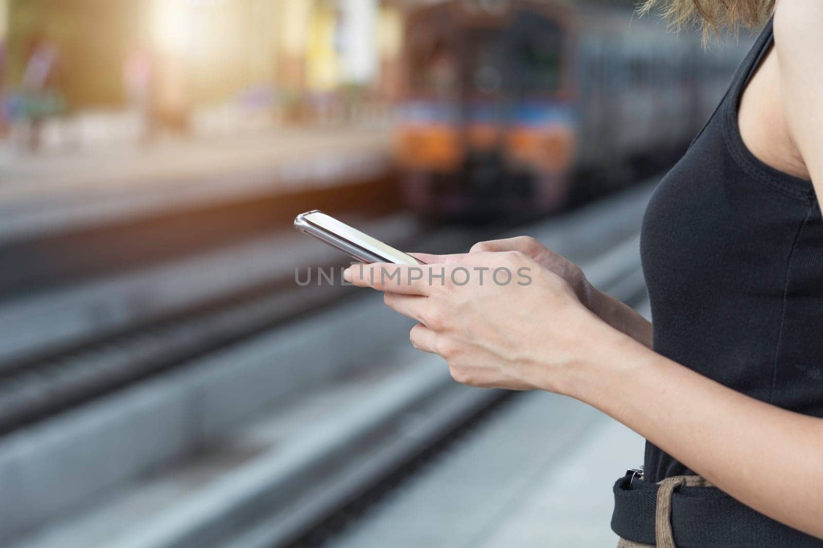 Woman standing and waiting for train and using smart phone in train station. Travel concept.