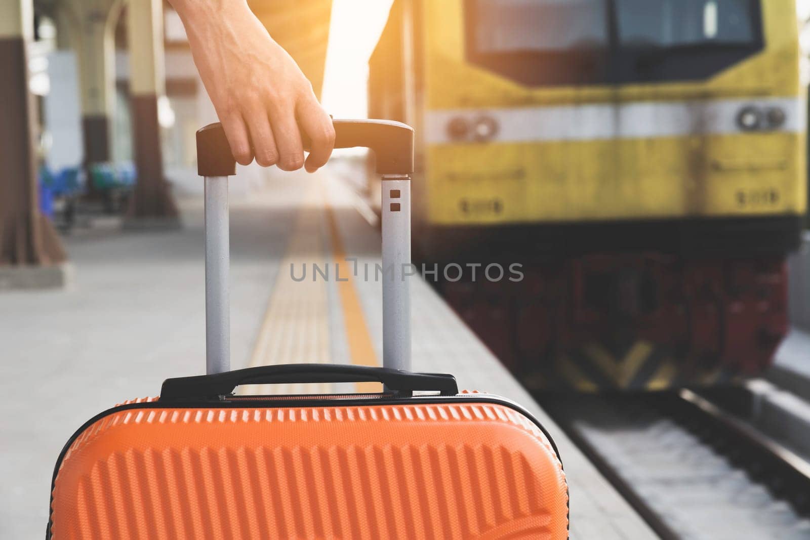Woman dragging orange suitcase luggage bag, walking in train station. Travel concept.