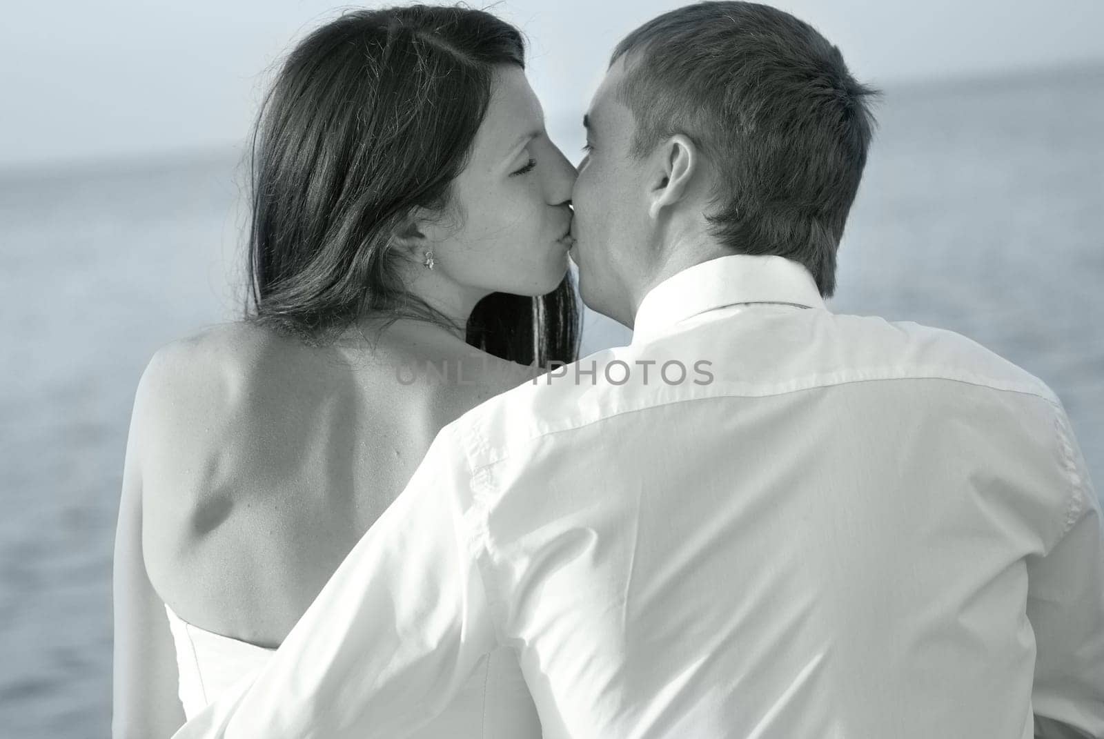 Beautiful wedding couple - bride and groom kissing at the beach. Just married. Black and white