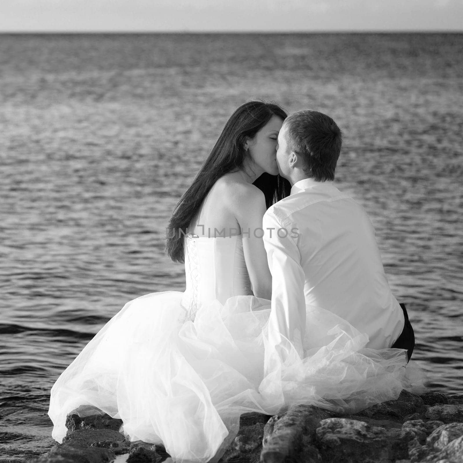 Beautiful wedding couple - bride and groom kissing at the beach. Just married. Black and white
