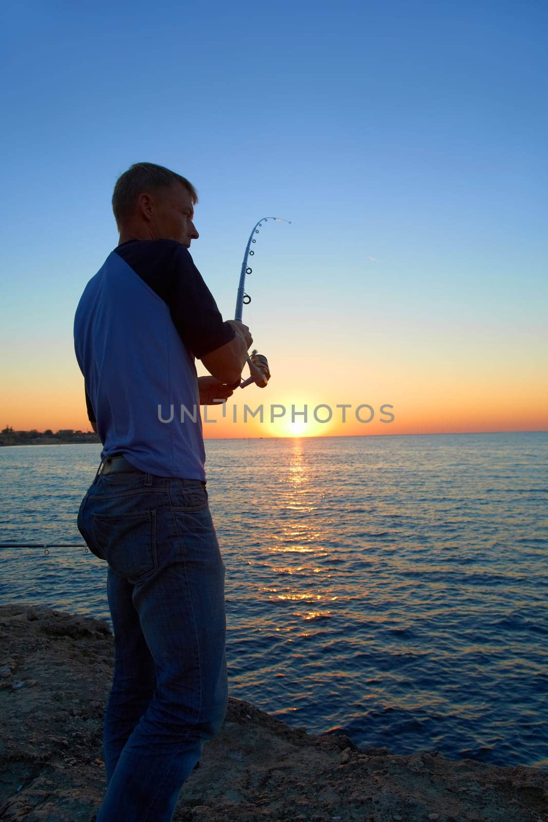 Fisherman fishes on the lake. Silhouette at sunset