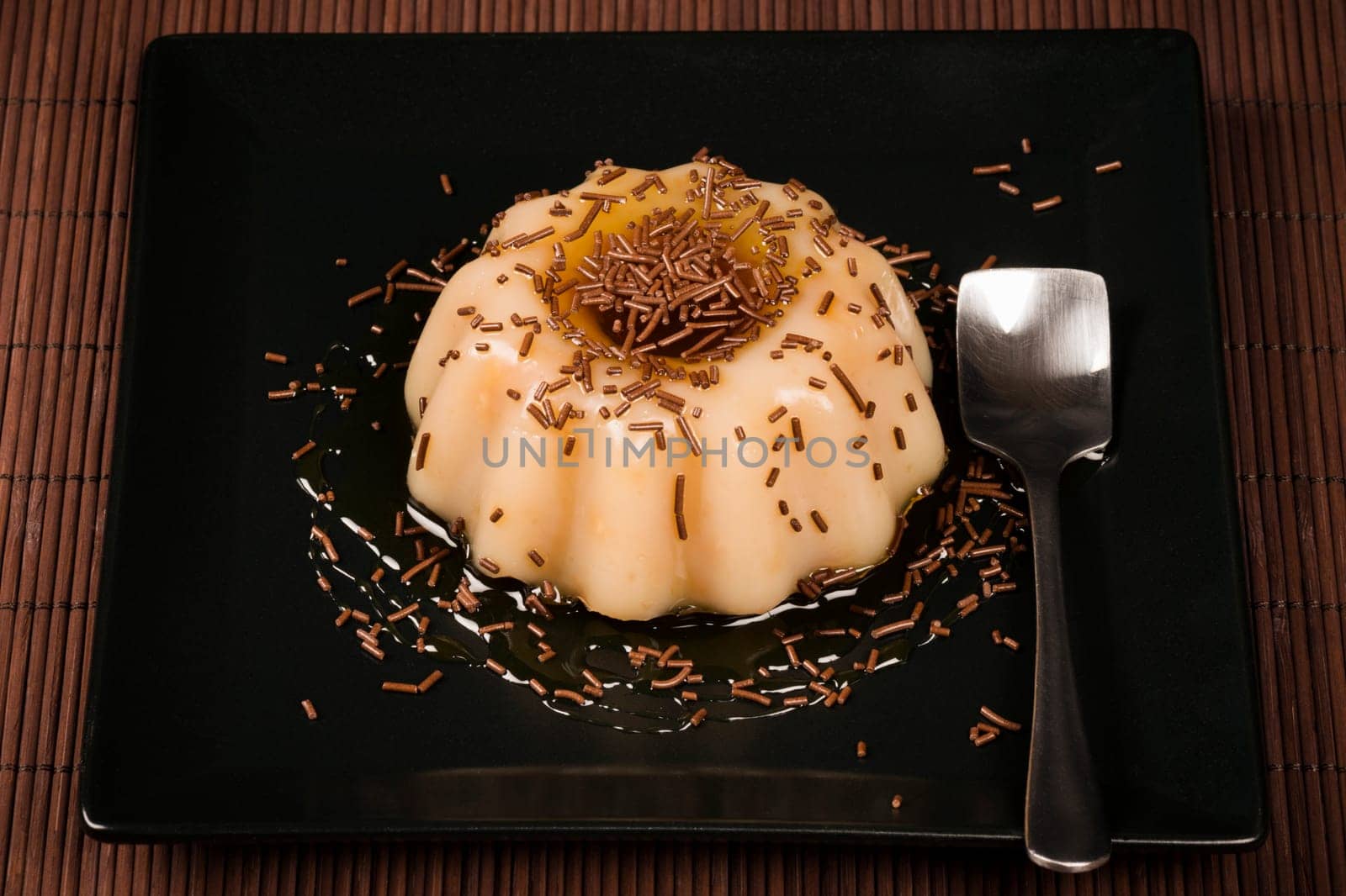 Cream pudding sweet dessert is served on black square shape plate on brown background.