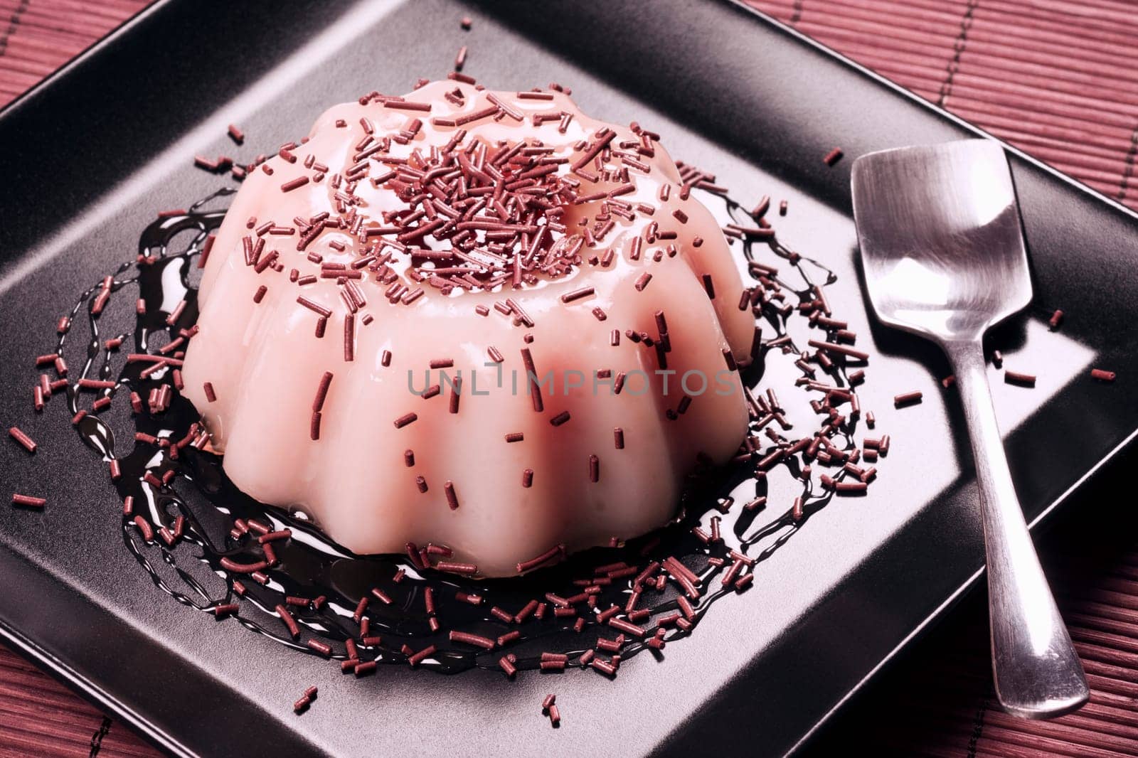 Pink pudding dessert with strawberry or raspberry taste on black plate.