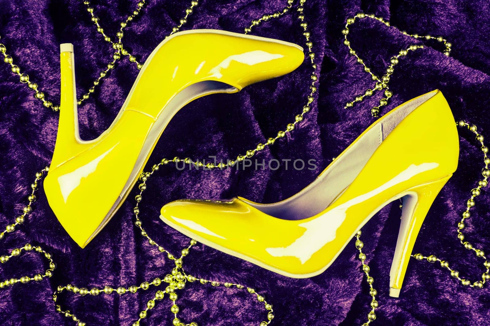 Sexy yellow high heels shoes are on dark purple fur background with yellow pearl jewelry.