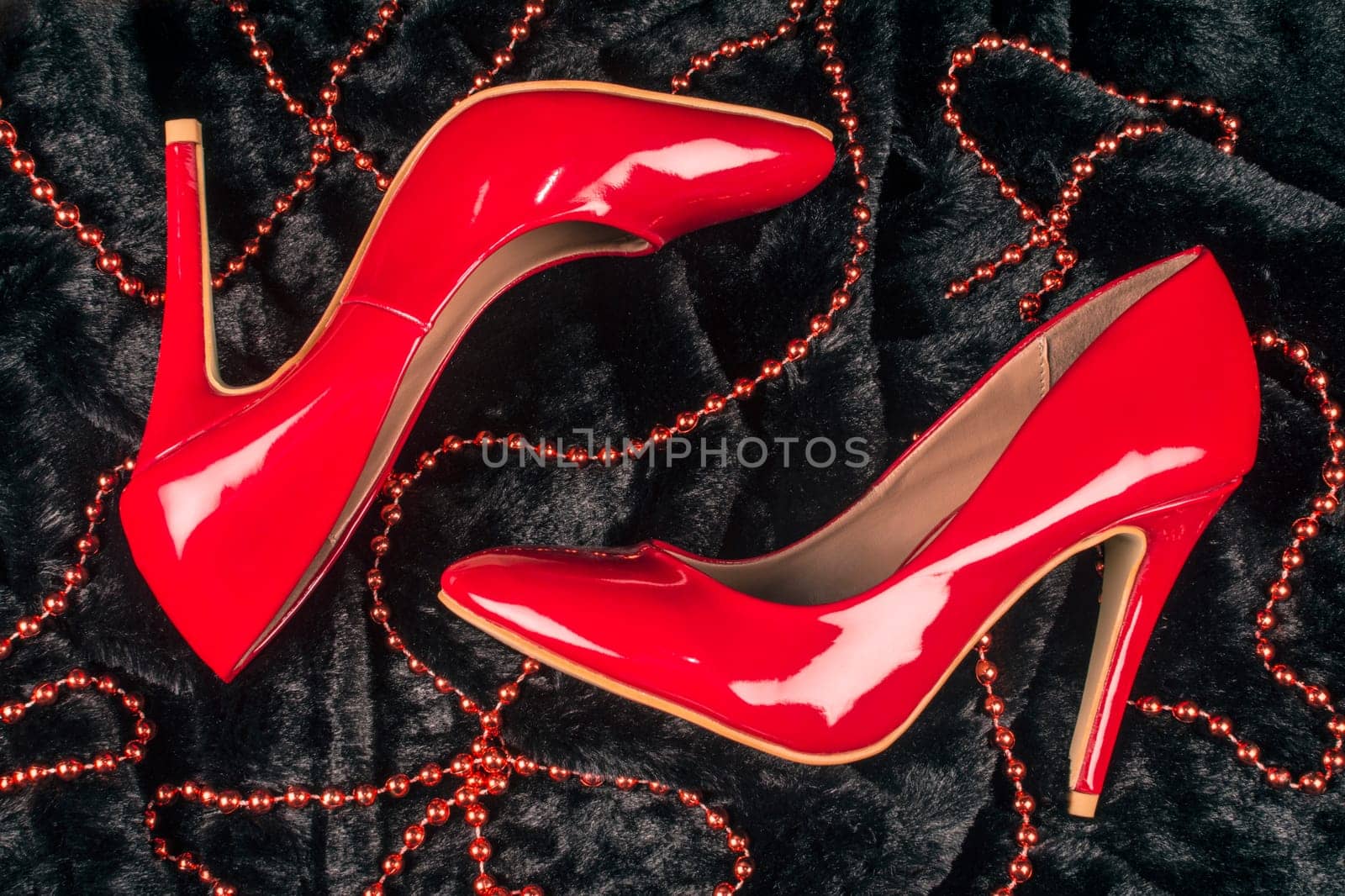 Sexy red high heels shoes are on black fur background with red pearl jewelry.