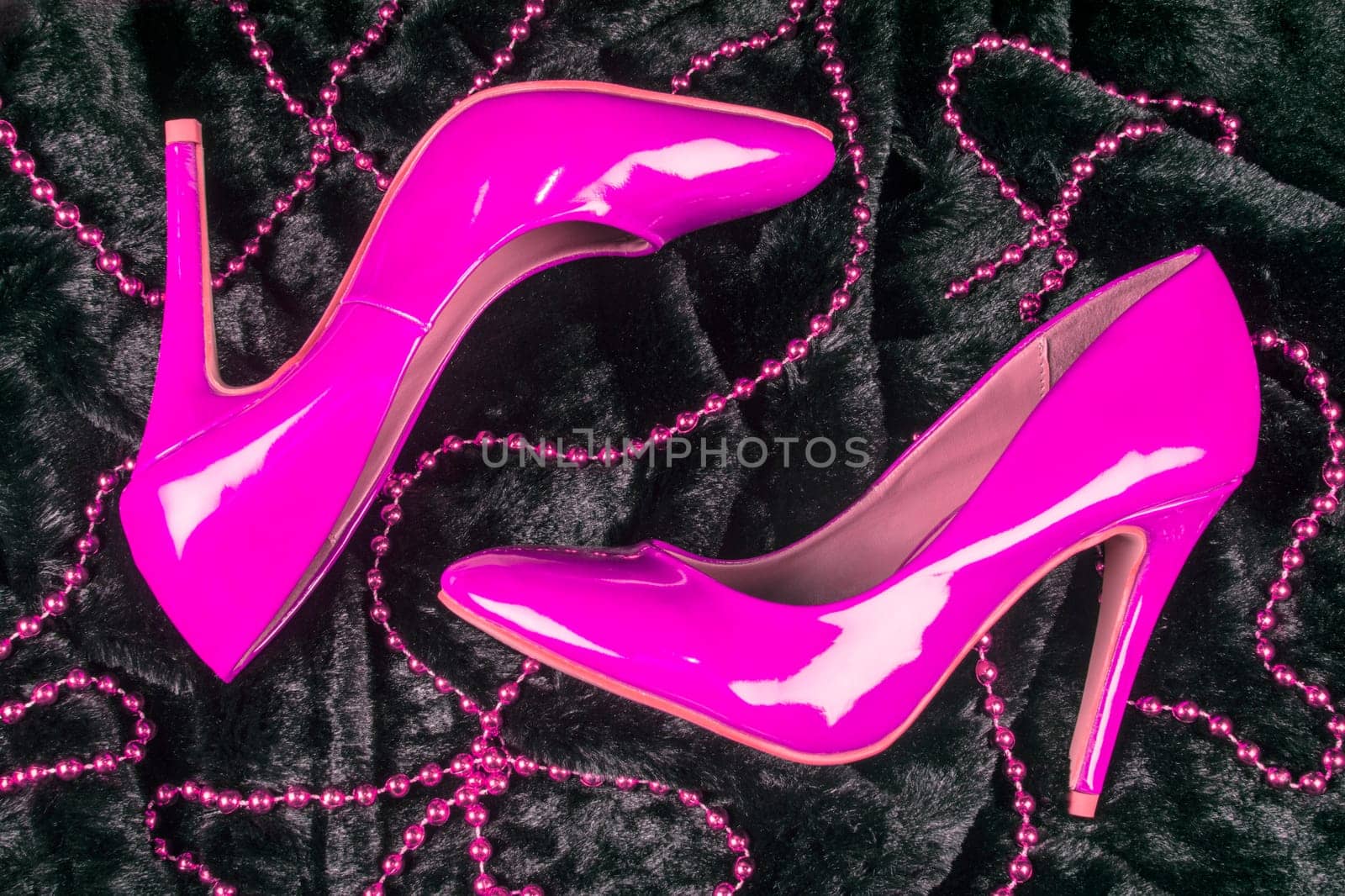 Sexy pink high heels shoes are on black fur background with pink pearl jewelry.
