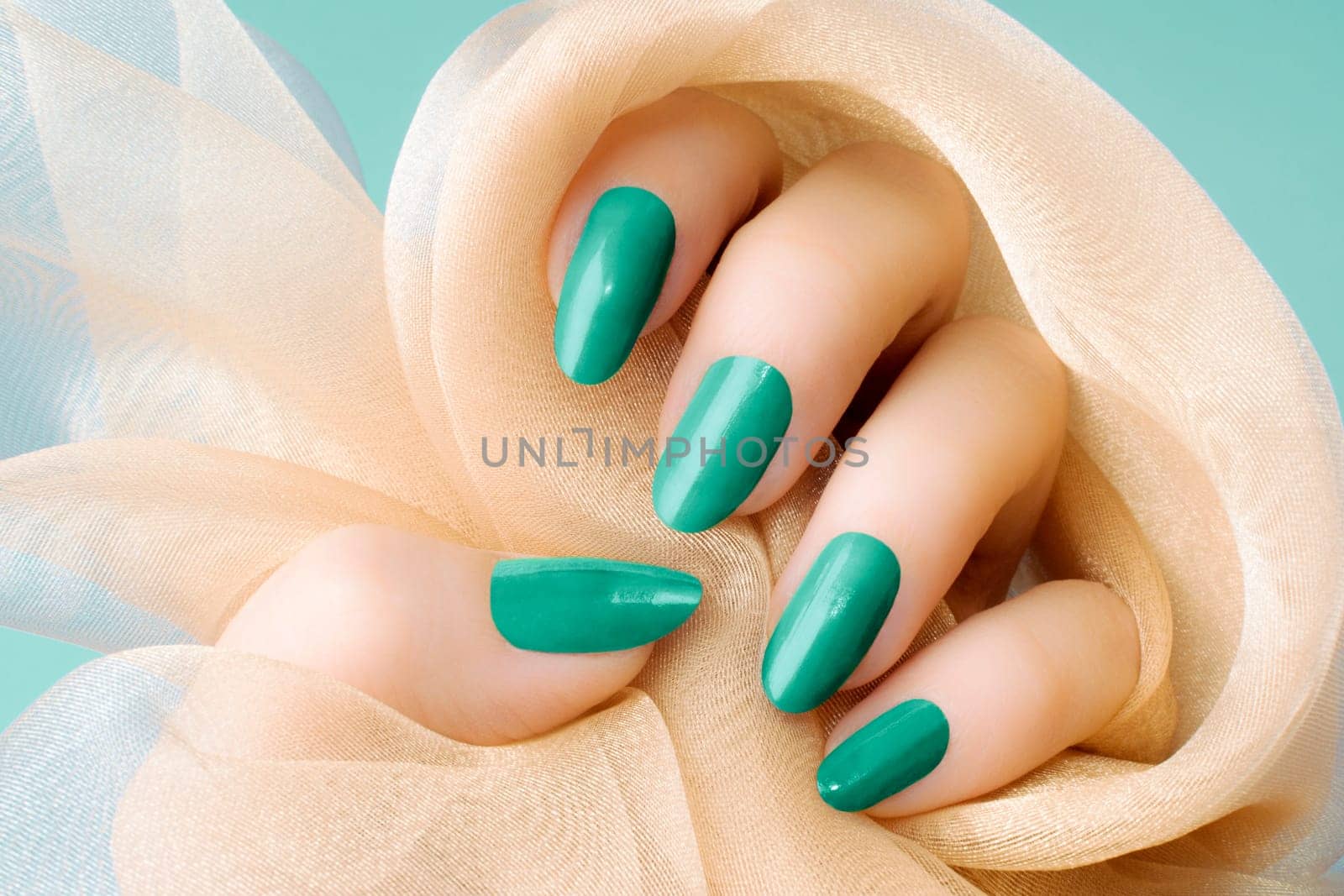 Female hand with turquoise nails is holding beige textile, nail care and manicure concept.