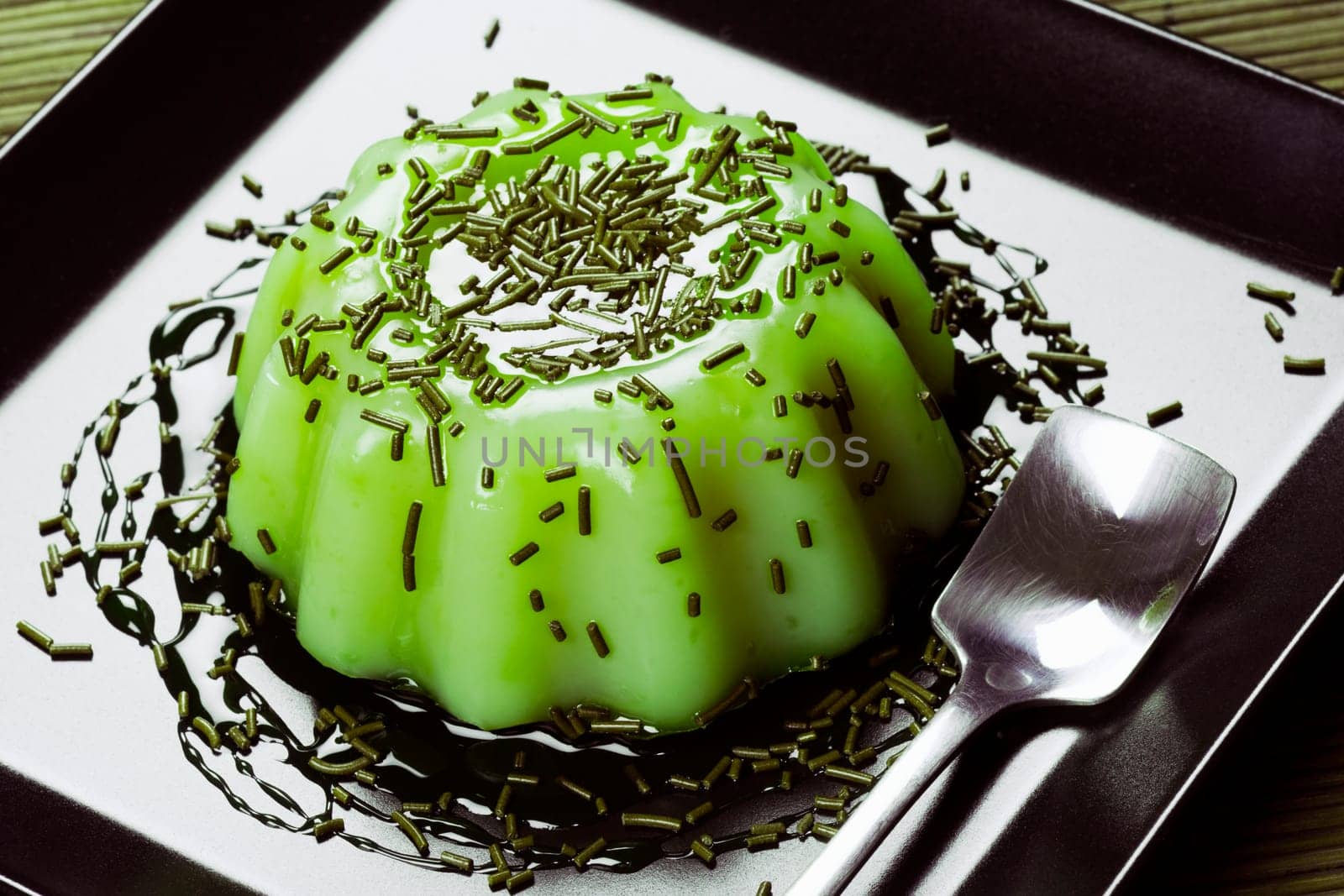 Green pudding sweet dessert from kiwi is served on black plate.