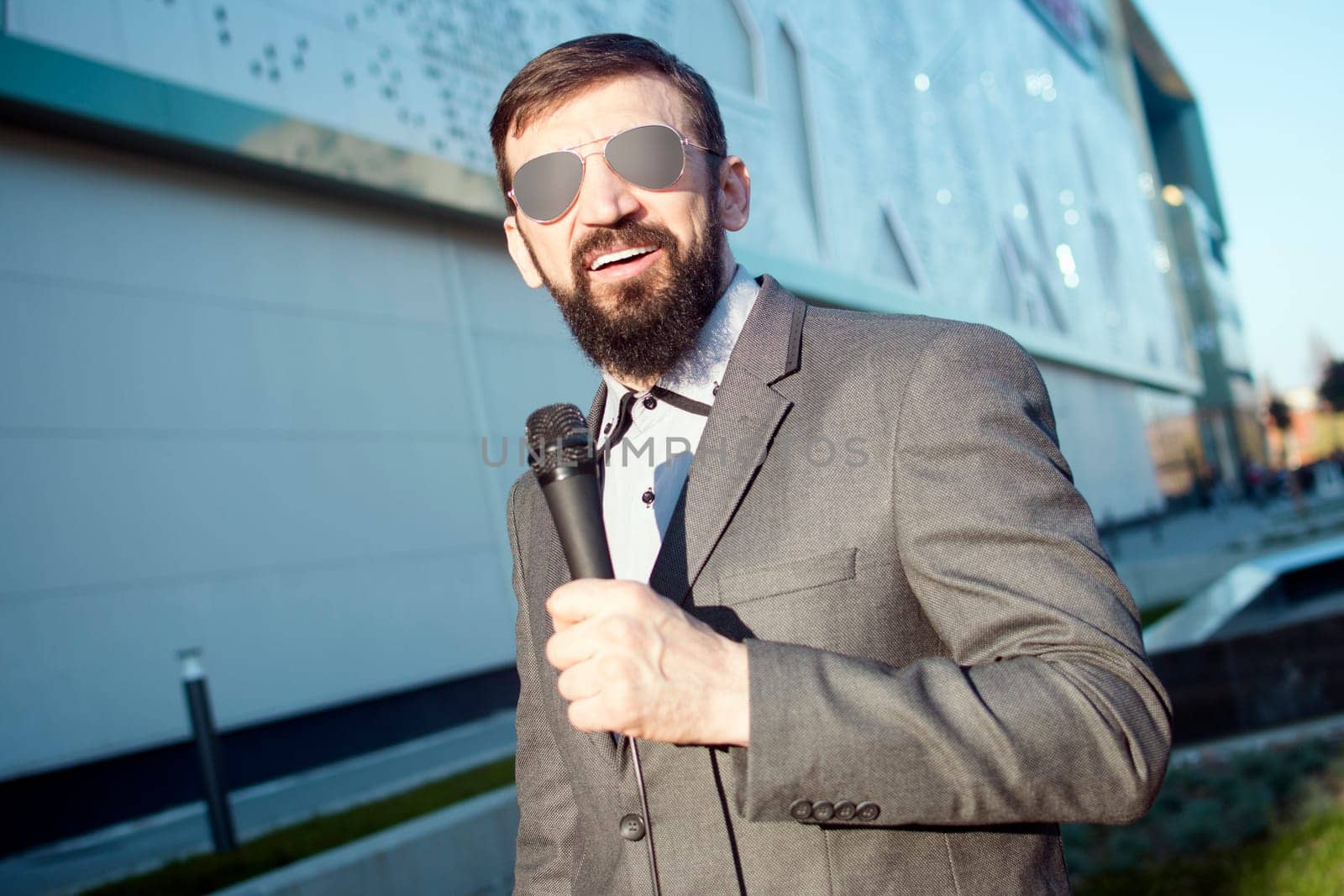 The bearded anchorman with microphone is presenting daily news in live program at the street.