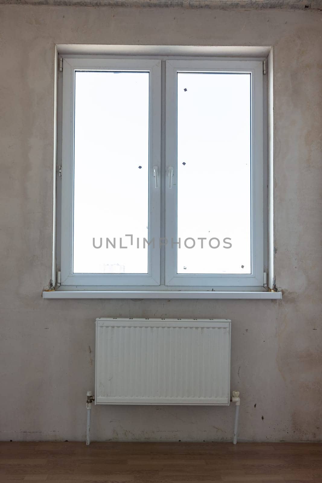 View of the window and the battery under the window in the interior of an unrepaired room