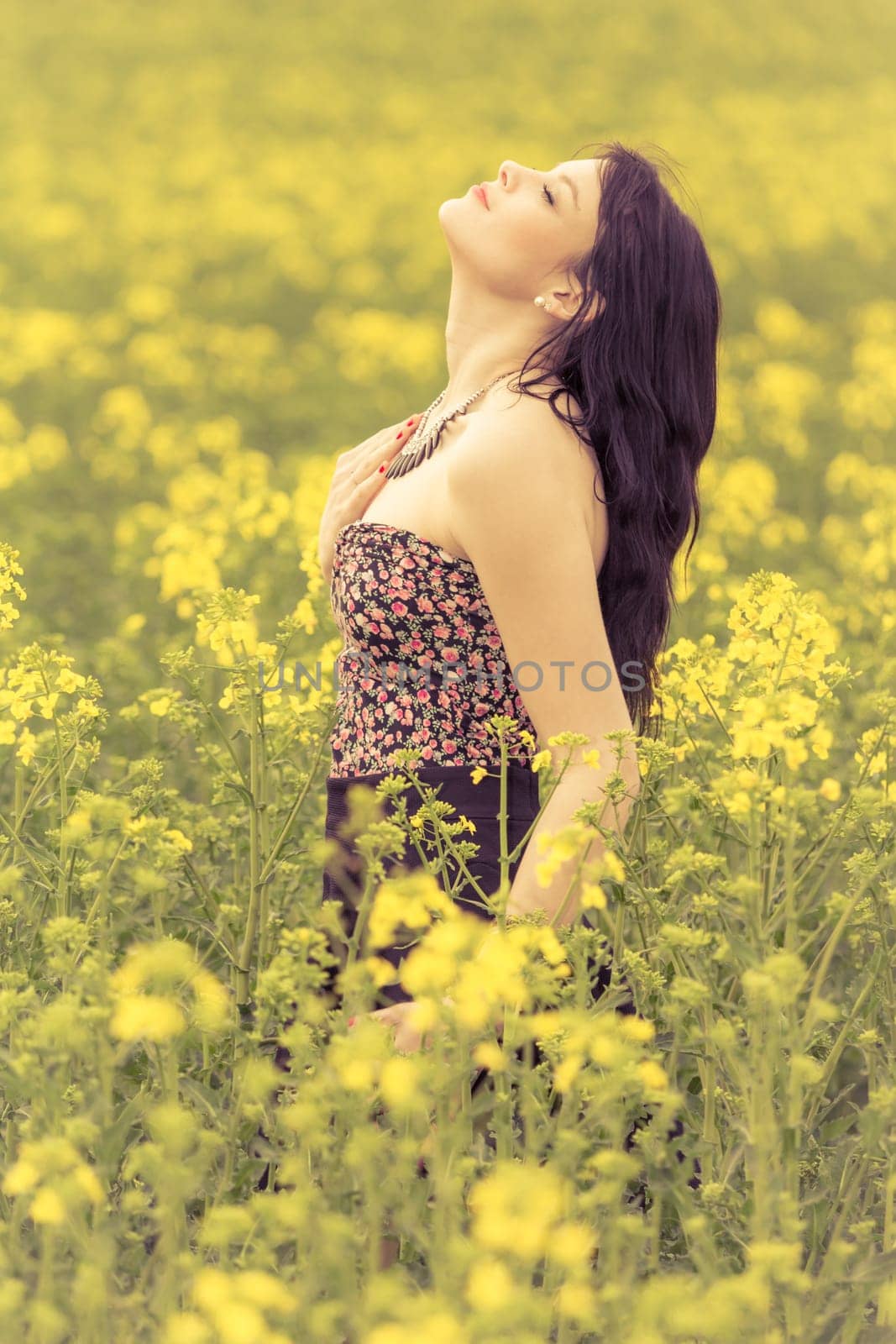 Attractive young beauty girl enjoying the warm sunny sun in nature rapeseed field takes time feeling sustainability and contemplation.