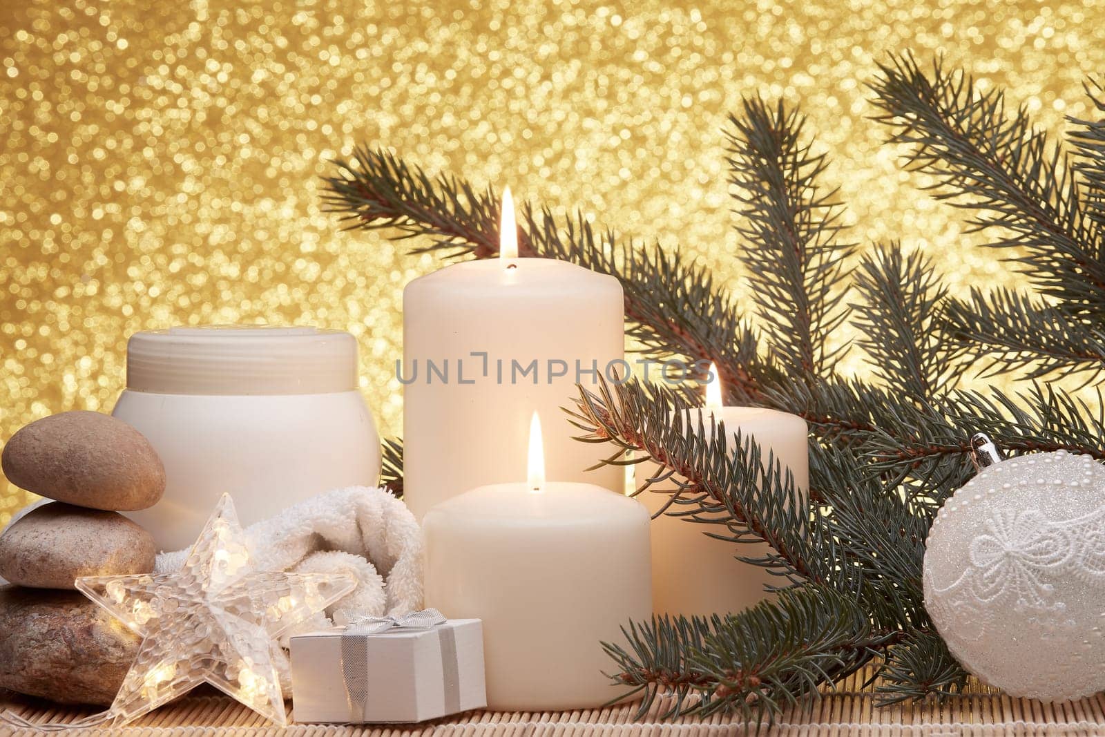 Spa still life with cosmetic creams, candles, fir branches, gift boxes and Christmas ornaments on a gold background. New Year and Christmas vacation. Healthy lifestyle, body care, Spa treatment and relaxation concept.