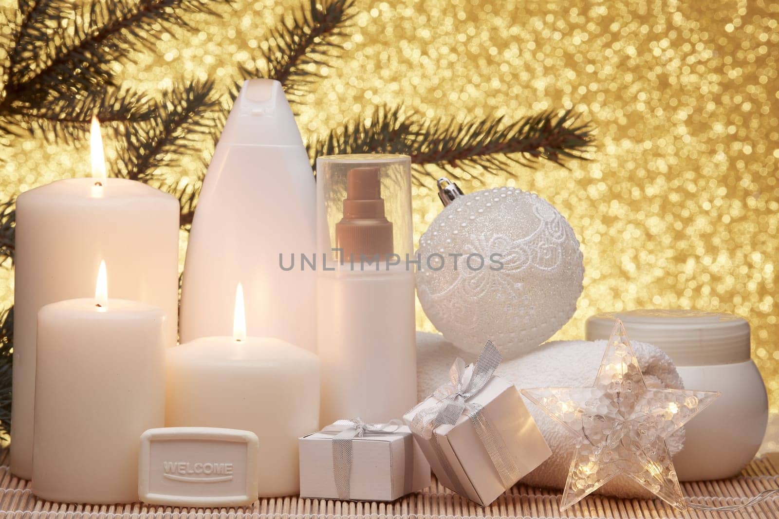 Spa still life with cosmetic creams, candles, fir branches, gift boxes and Christmas ornaments on a gold background. New Year and Christmas vacation. Healthy lifestyle, body care, Spa treatment and relaxation concept.