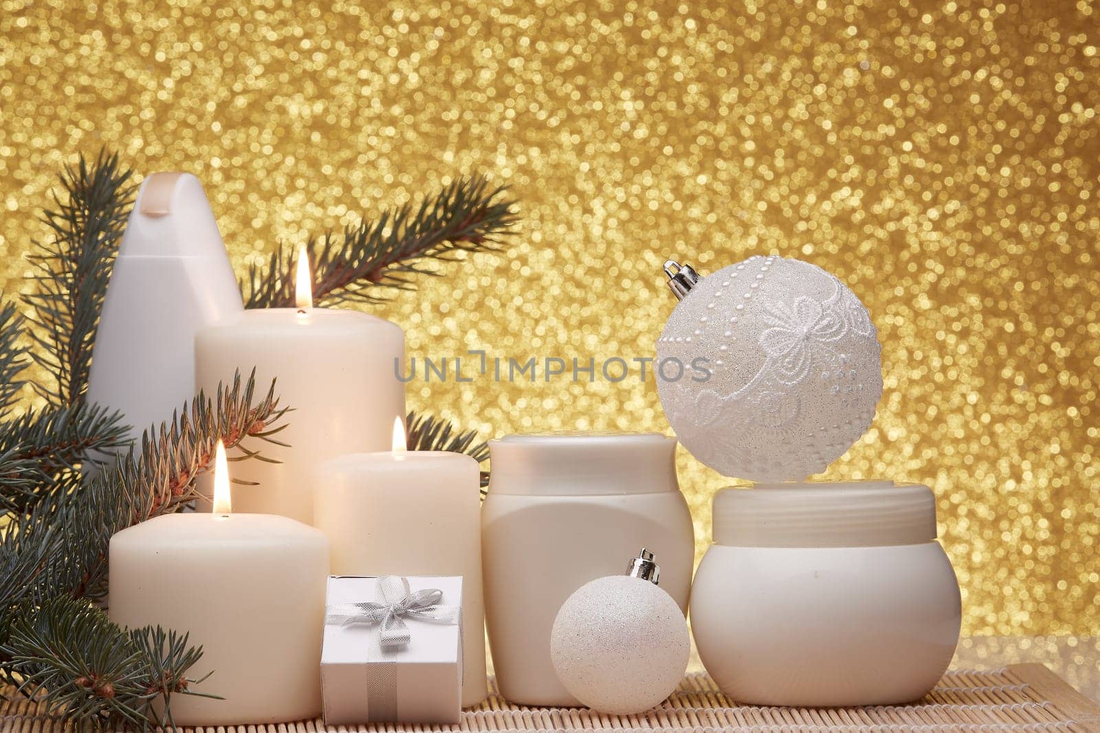 Spa still life with cosmetic creams, candles, fir branches, gift boxes and Christmas ornaments on a gold background. New Year and Christmas vacation. Healthy lifestyle, body care, Spa treatment and relaxation concept.