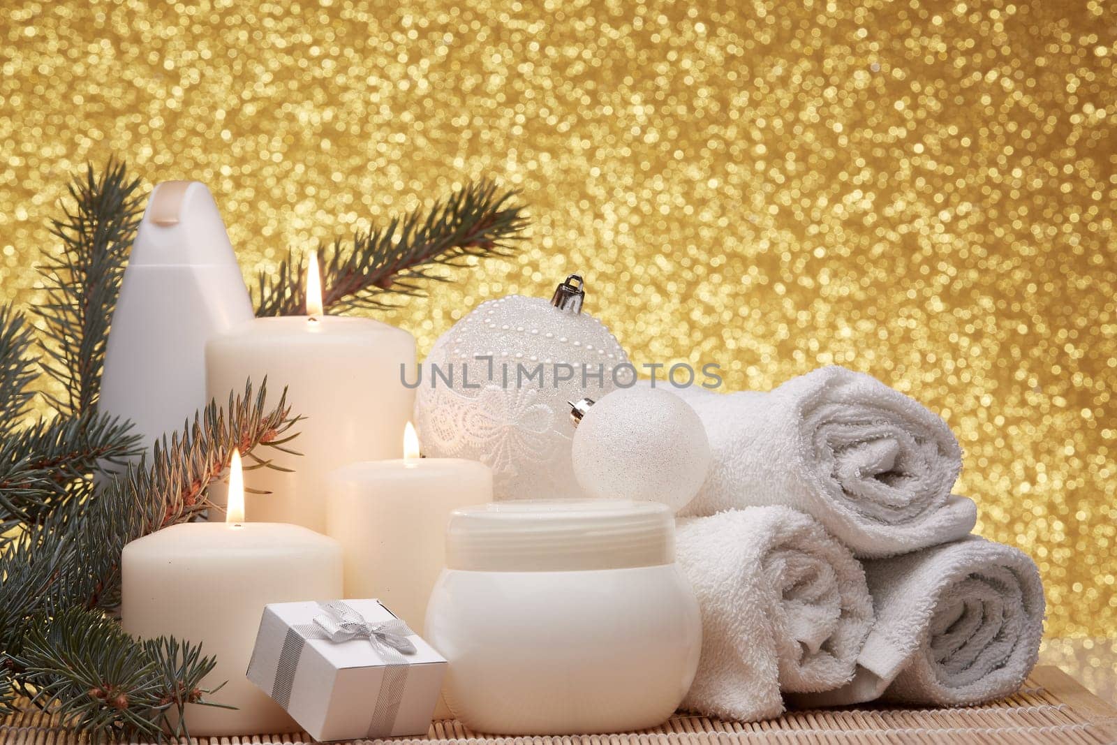 Spa still life with cosmetic creams, candles, fir branches, gift boxes and Christmas ornaments on a gold background. New Year and Christmas vacation. Healthy lifestyle, body care, Spa treatment and relaxation concept.