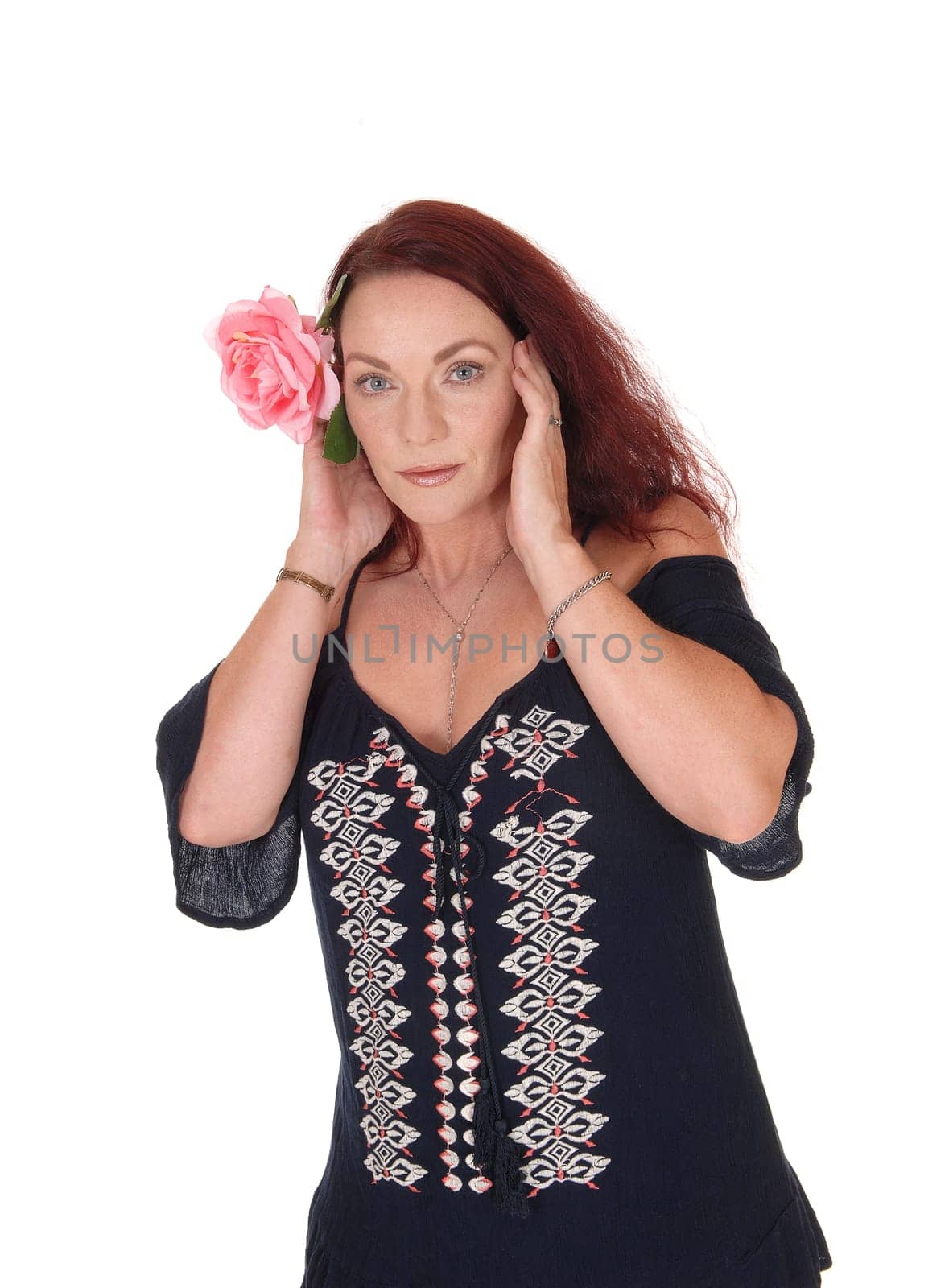 A waist up picture of a pretty woman with long red hair holding one.pink rose on her hair, looking serious, isolated for white background.