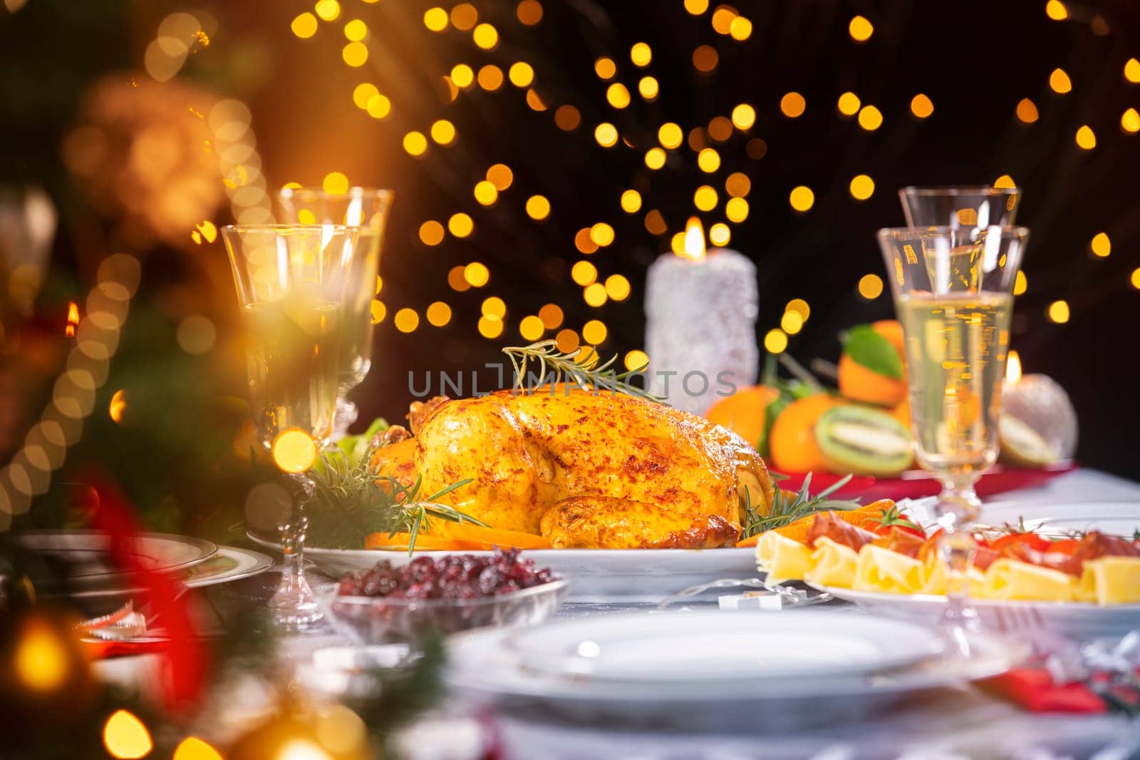 Christmas dinner. Closeup photo of tasty baked chicken against glowing Christmas lights and burning candles. Holiday decorated table, Christmas tree, champagne and roasted turkey, Christmas served table.