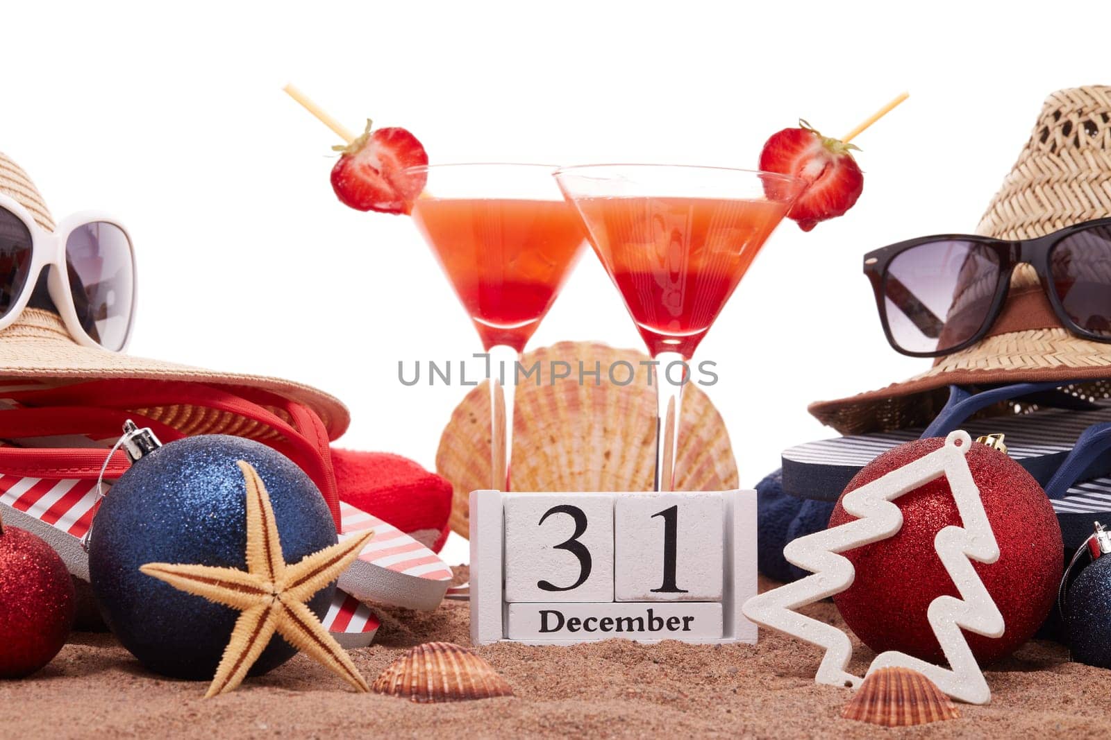 Beach accessories (flip flops, straw hats, seashells, sand, sunglasses), two glasses of cocktail, christmas ornaments on white background. New Year. Winter vacation in warm countries, beach holiday