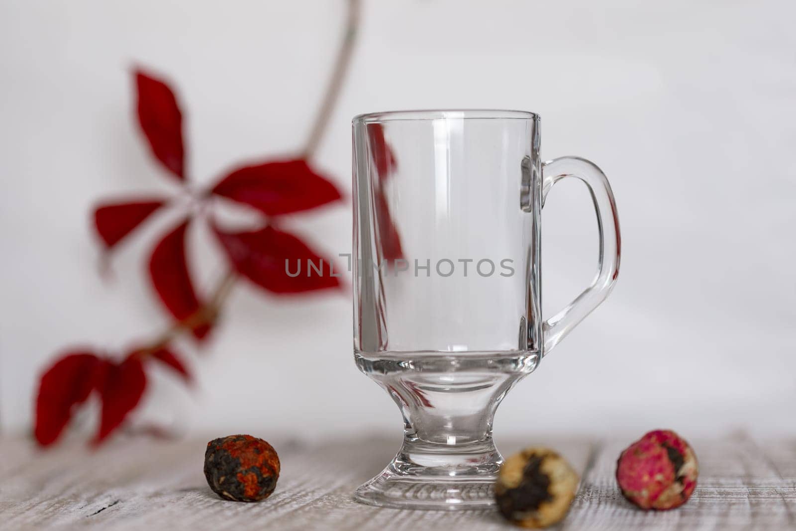 Red autumn leaf on a branch with an empty glass and balls of Chinese tea on a white and wooden backgroundRed autumn leaf on a branch on a white and wooden background , background for copy space
