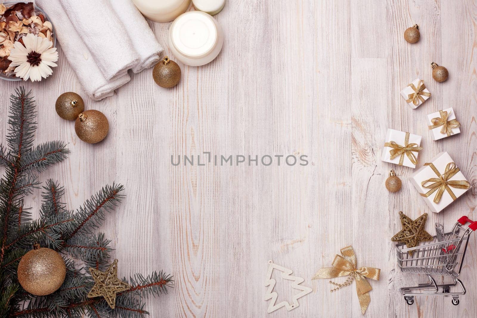 Shopping trolley with gift boxes, spa composition with cosmetic creams, towel and Christmas ornaments on light wooden background. Top view with copy space. Christmas and New Year sale.
