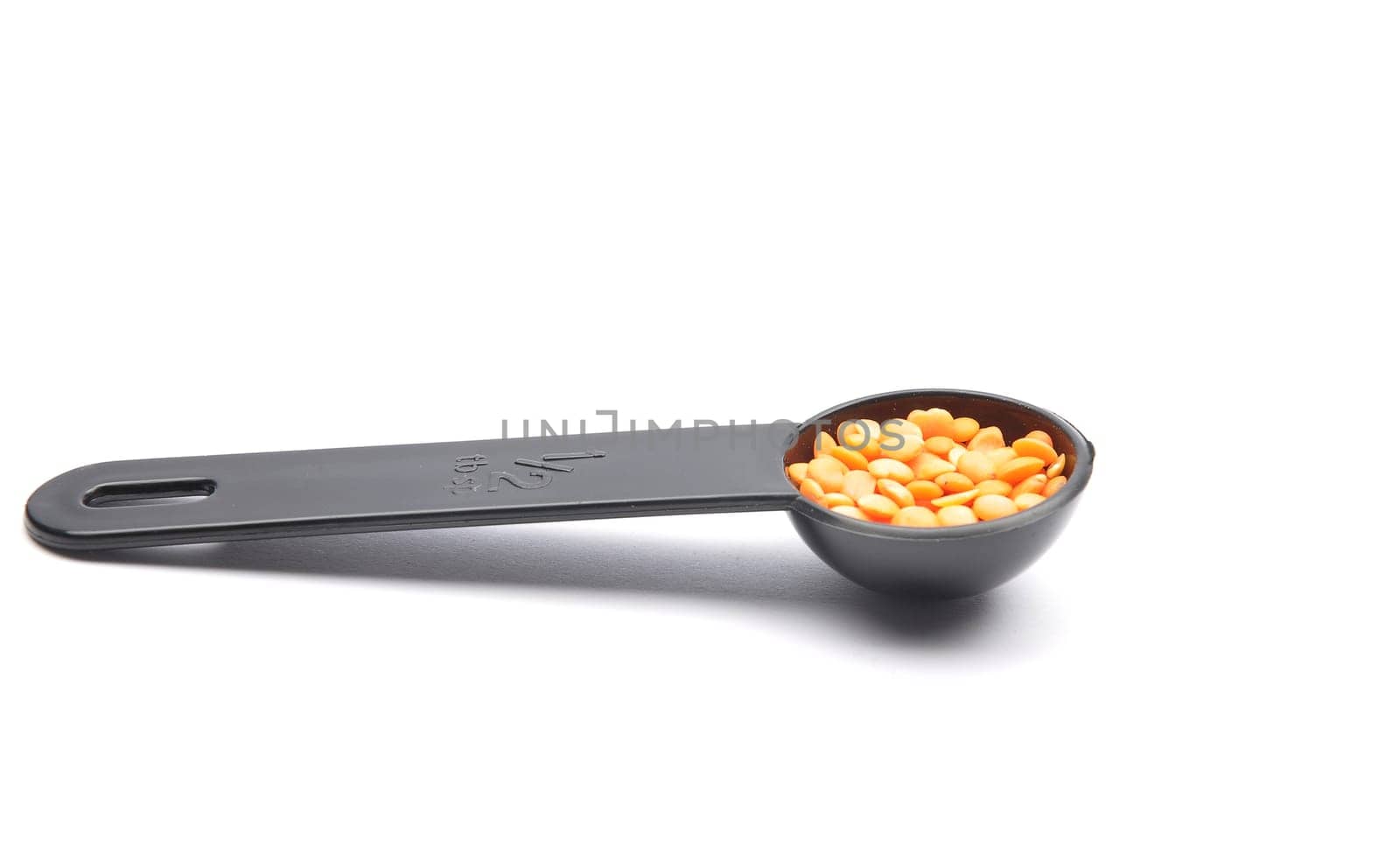 Red lentils on measuring spoon and white background