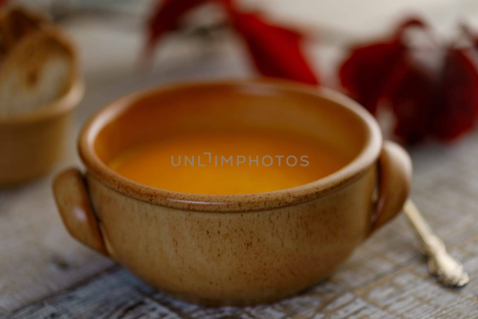 Pumpkin cream soup in a ceramic dish with breadcrumbs and red autumn leaves in the background