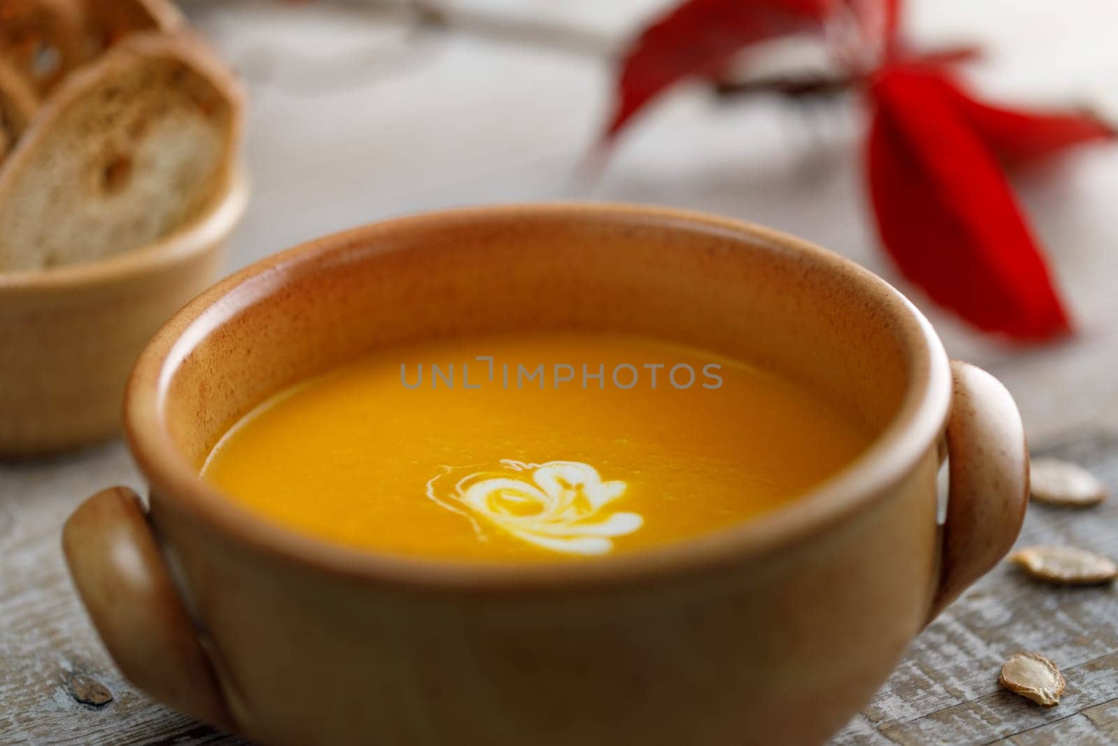 Pumpkin cream soup in a ceramic dish with breadcrumbs and red autumn leaves in the background