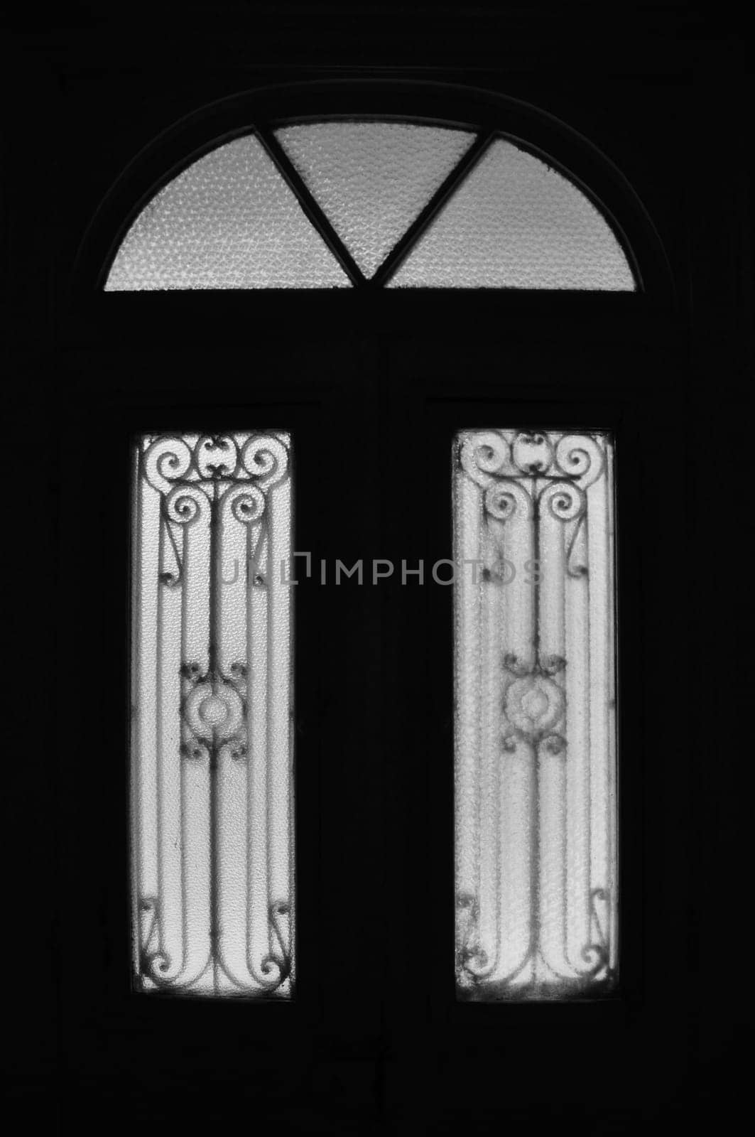 Vintage door frame with decorative motif and arched glass lite. Abandoned neoclassical house dark interior black and white.
