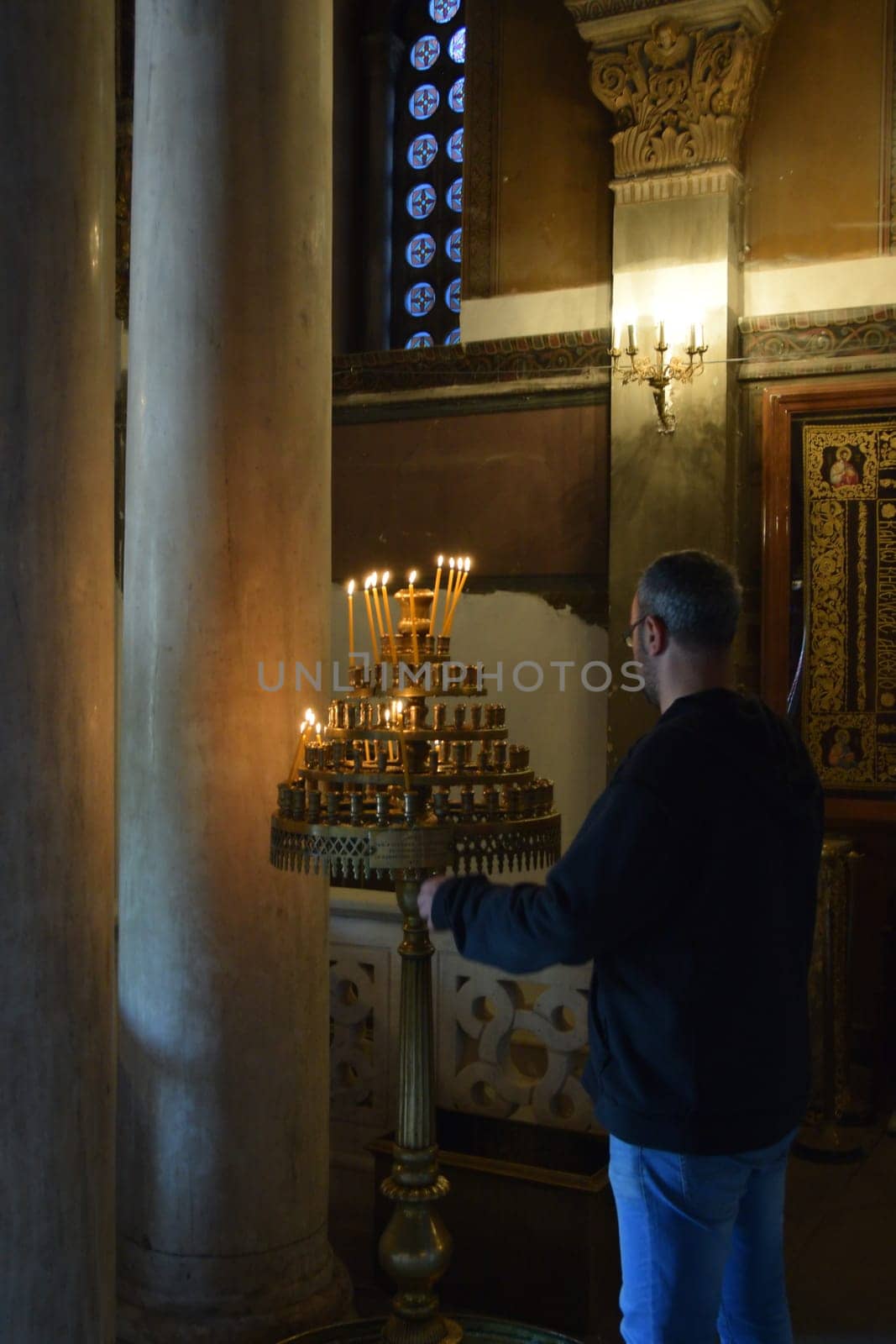 ATHENS, GREECE - APRIL 27, 2015: Man and antique manouali candle stand in byzantine church interior.