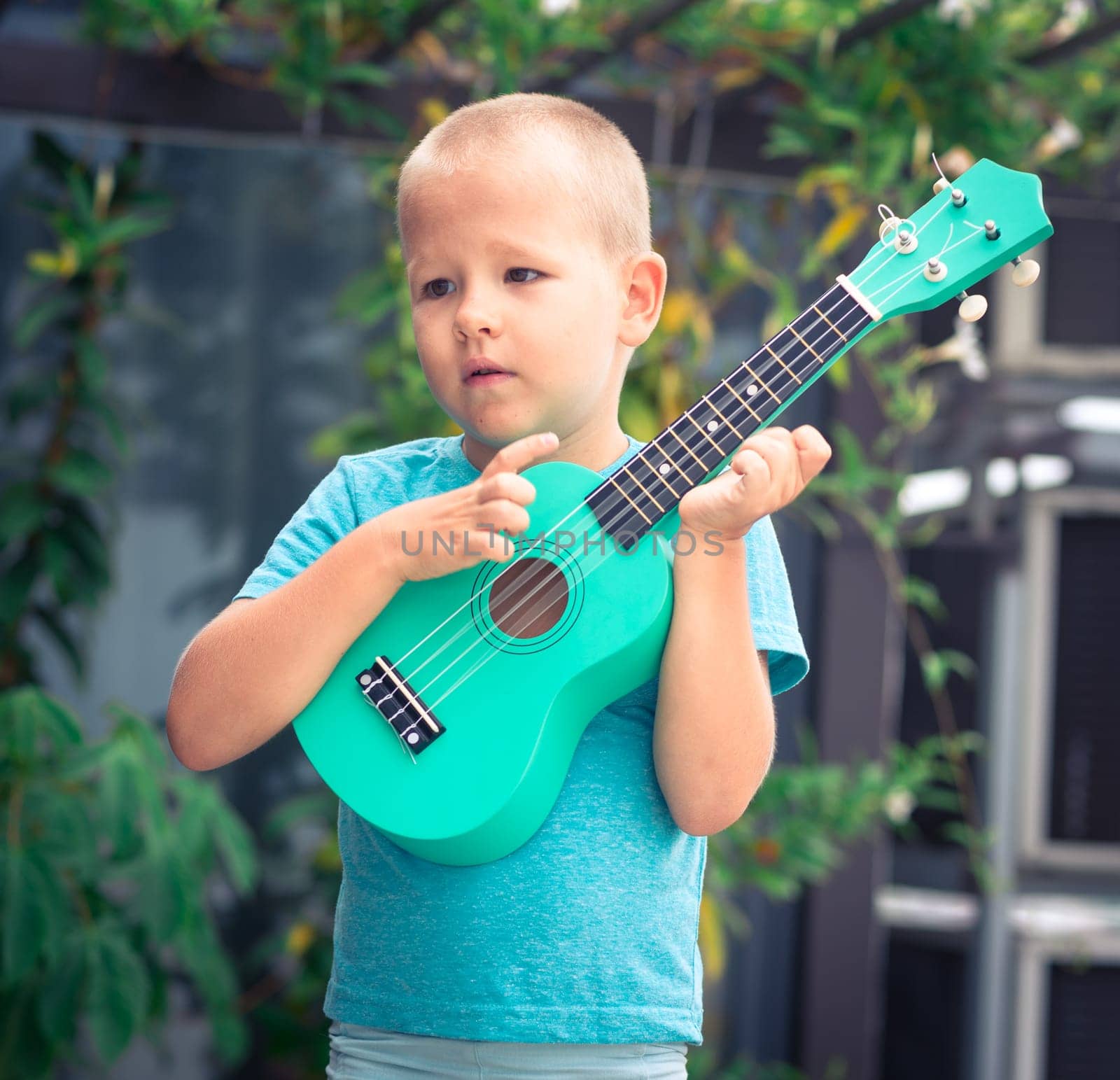 Portrait of a cute boy sitting ouddoor with ukulele