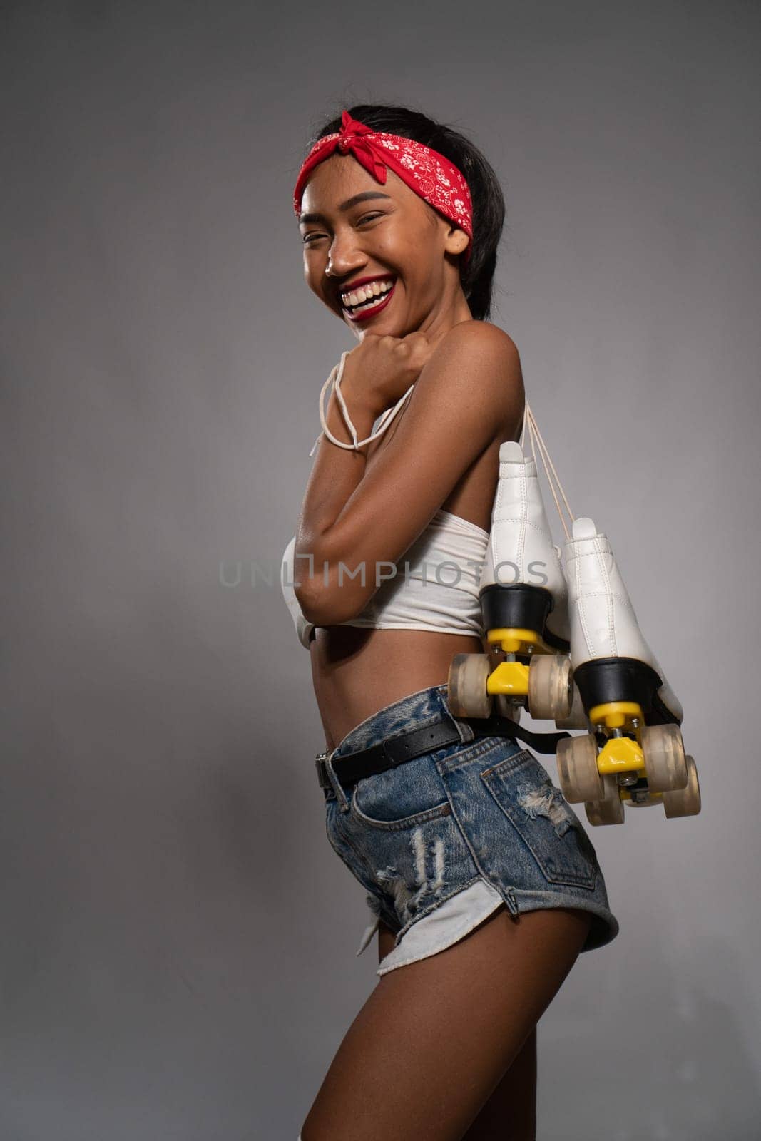 Young beautiful smiling Asian girl holding retro quads roller skates posing in studio over concrete wall background