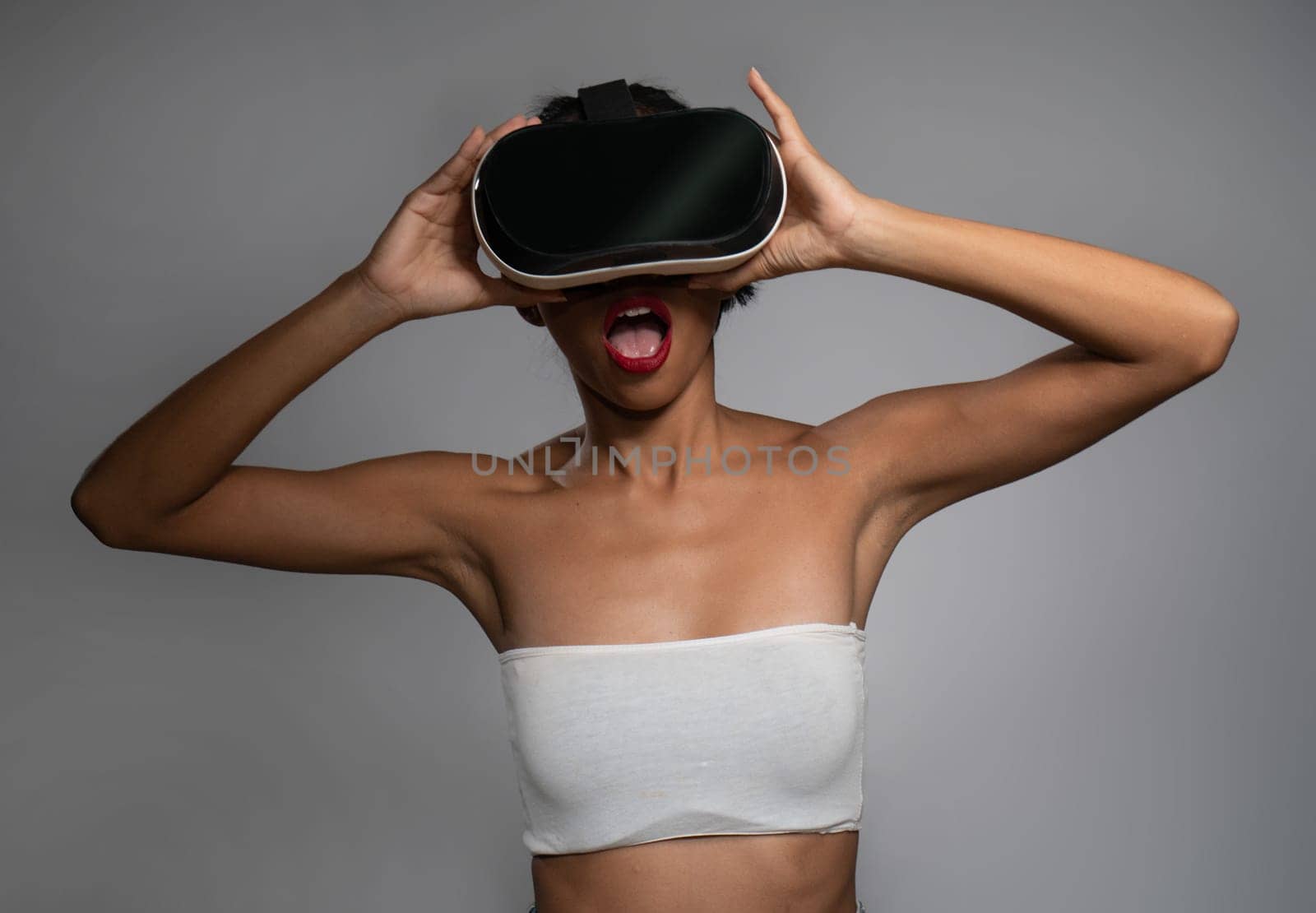 Pretty young Asian girl posing with virtual reality headset or 3d glasses isolated over gray wall background