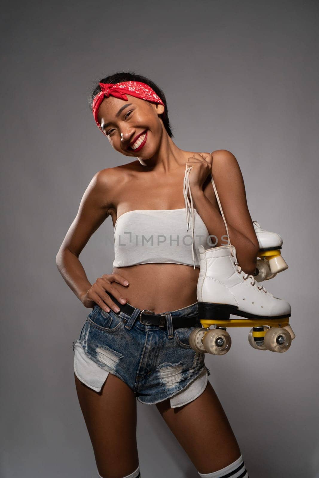 Young beautiful smiling Asian girl holding retro quads roller skates posing in studio over concrete wall background