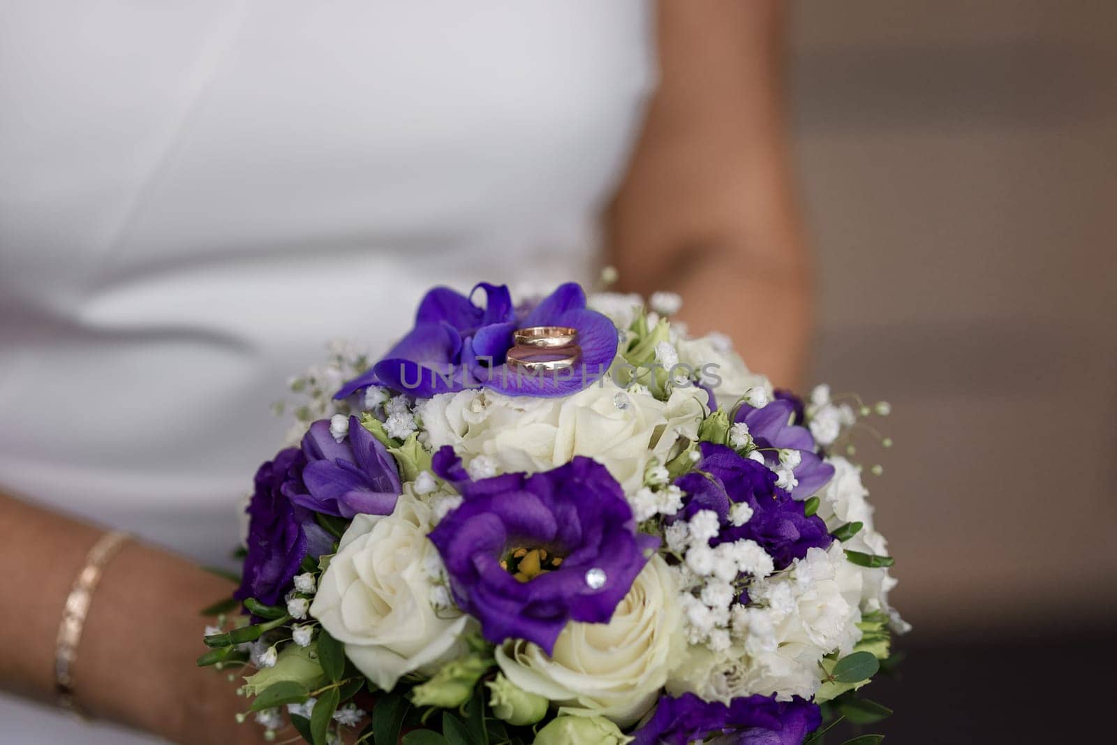 Wedding rings lying on the bride's bouquet of white and purple flowers in the hands of the bride