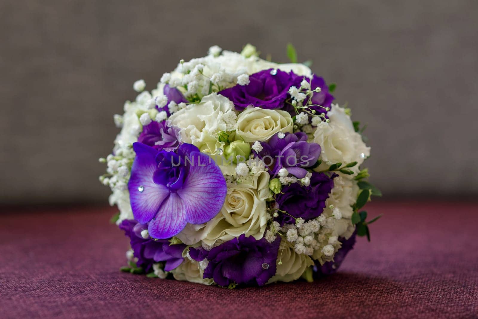 Bridal bouquet of white and purple flowers of round forim lying on the sofa with a large orchid flower
