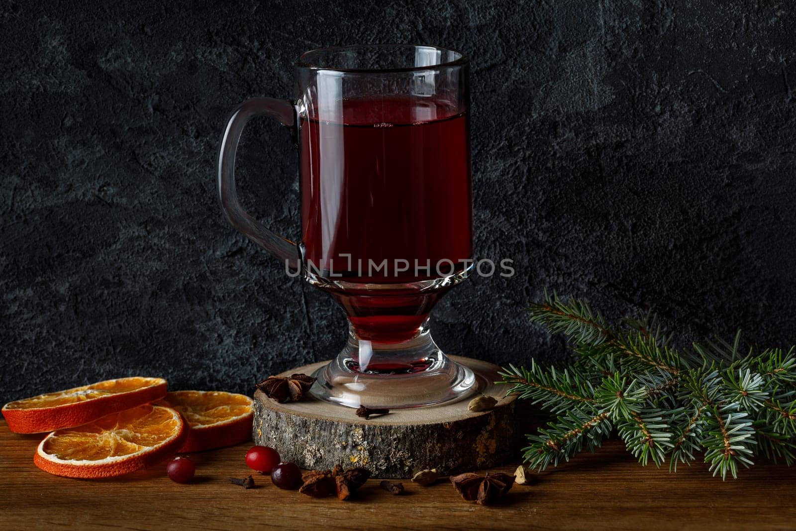 Mulled wine in a glass cup on a wooden platter, on the background of a fir branch and dry oranges