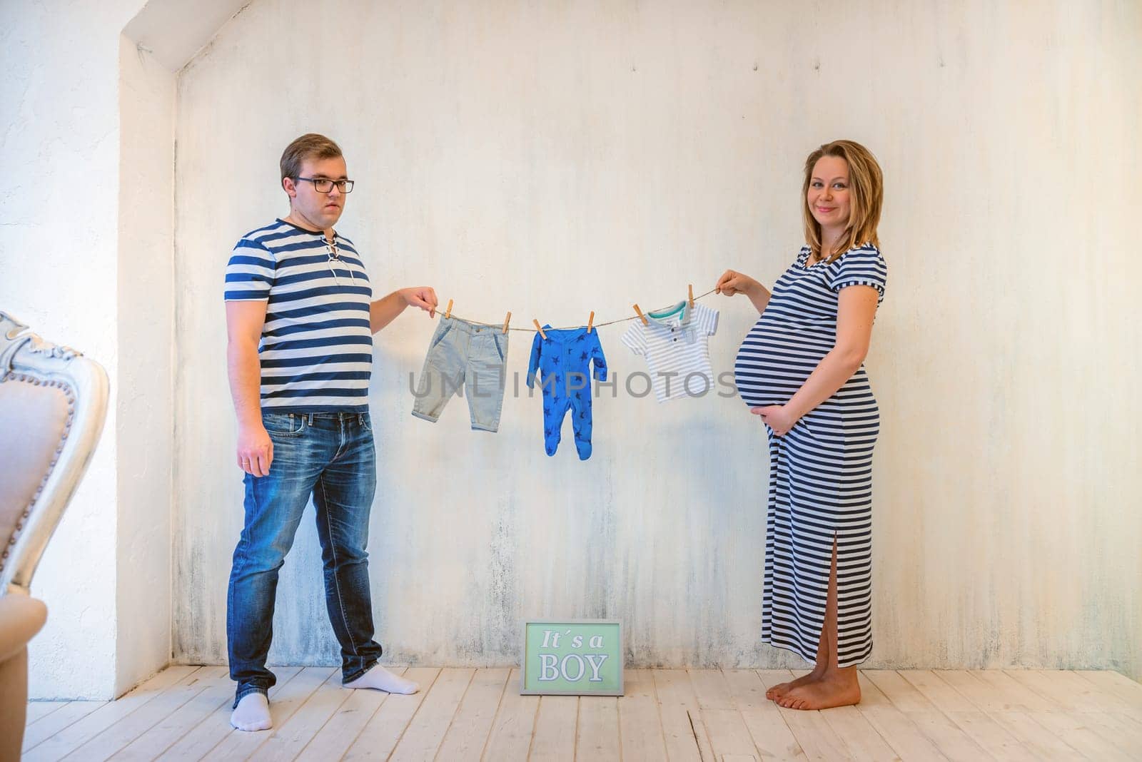 Young couple: pregnant woman and man holding baby clothes
