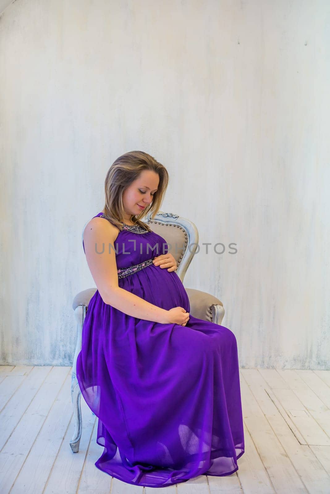 Beautiful pregnant woman in ultra violet dress sitting on the armchair
