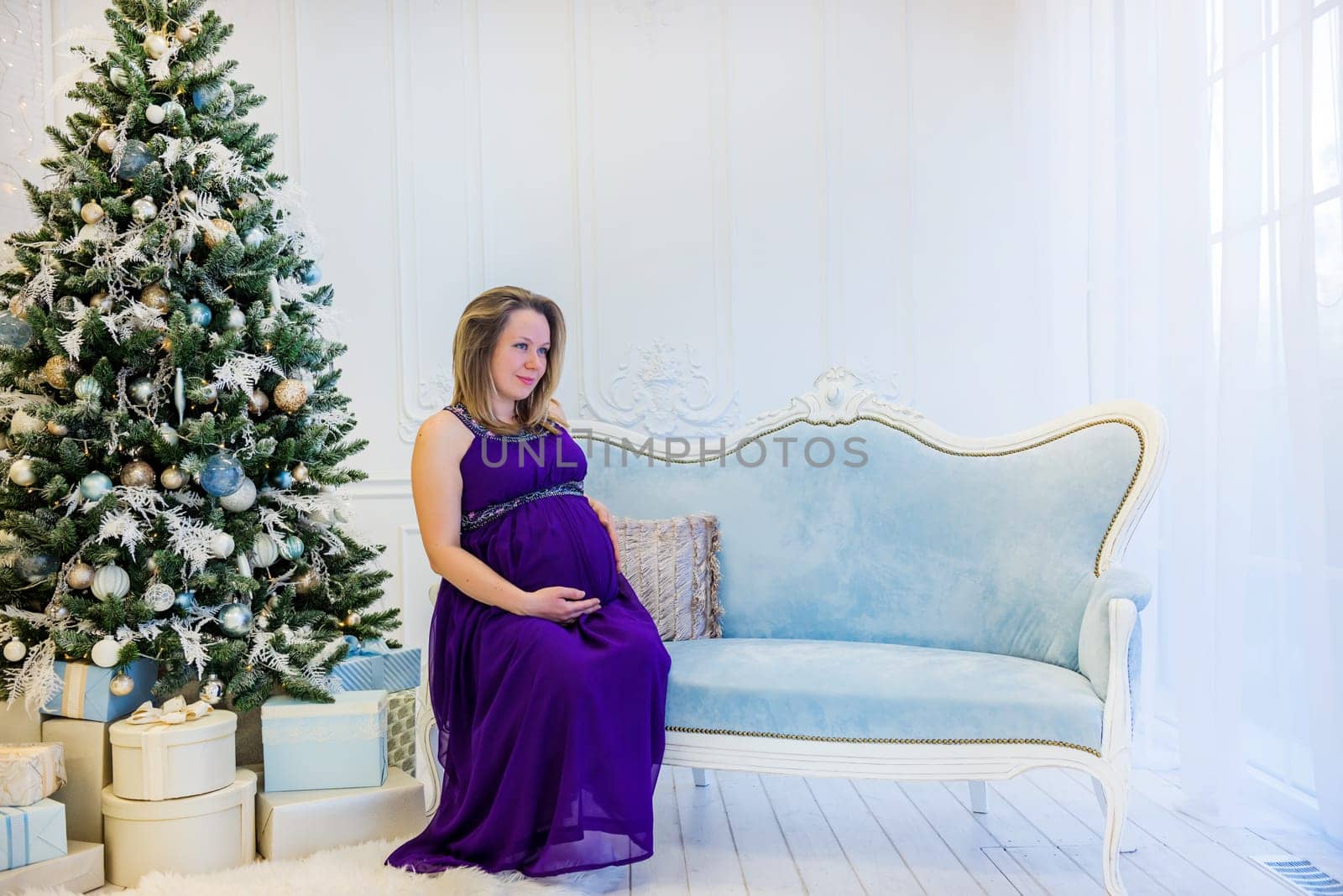 Beautiful pregnant woman in ultra violet dress sitting on the sofa