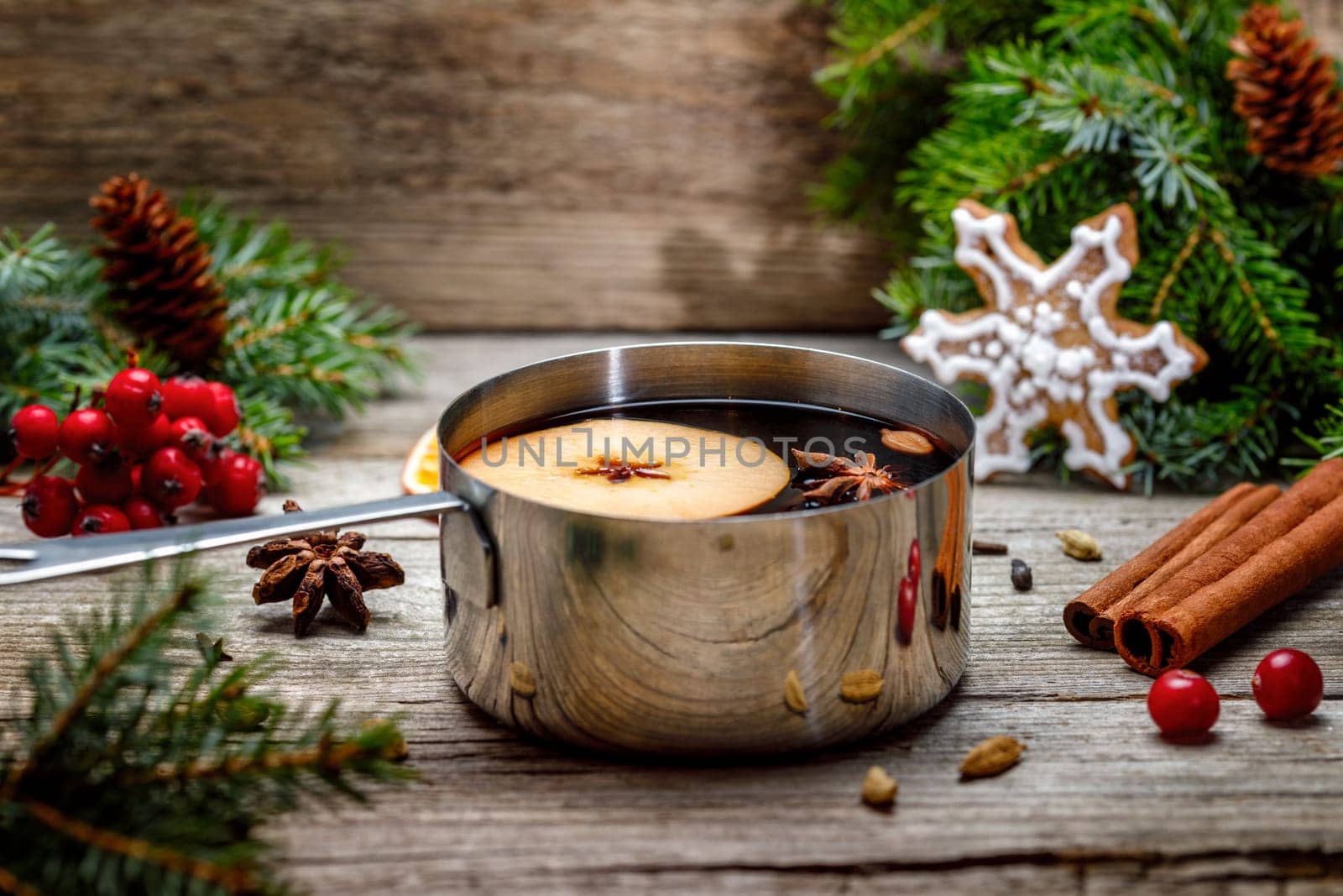 Small stewpot with mulled wine and cinnamon sticks, slice of oranges and apple on wooden table top view. Hot winter drink. Christmas beverage.