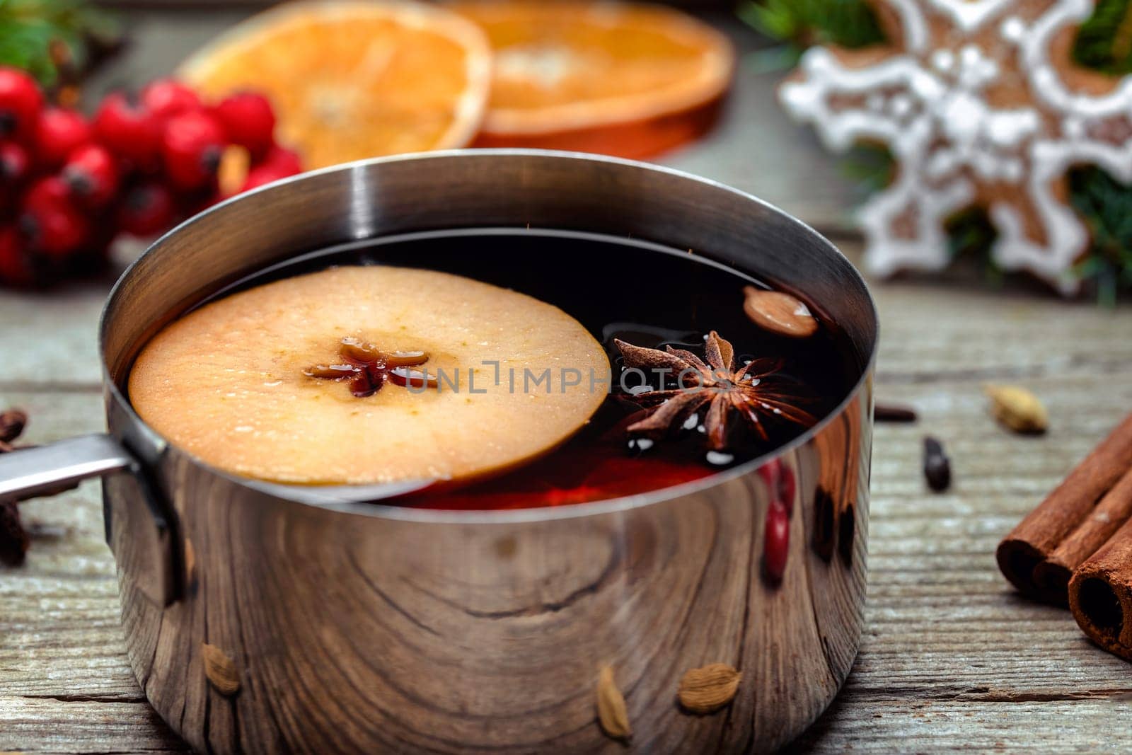 Small stewpot with mulled wine and cinnamon sticks, slice of oranges and apple on wooden table top view. Hot winter drink. Christmas beverage.