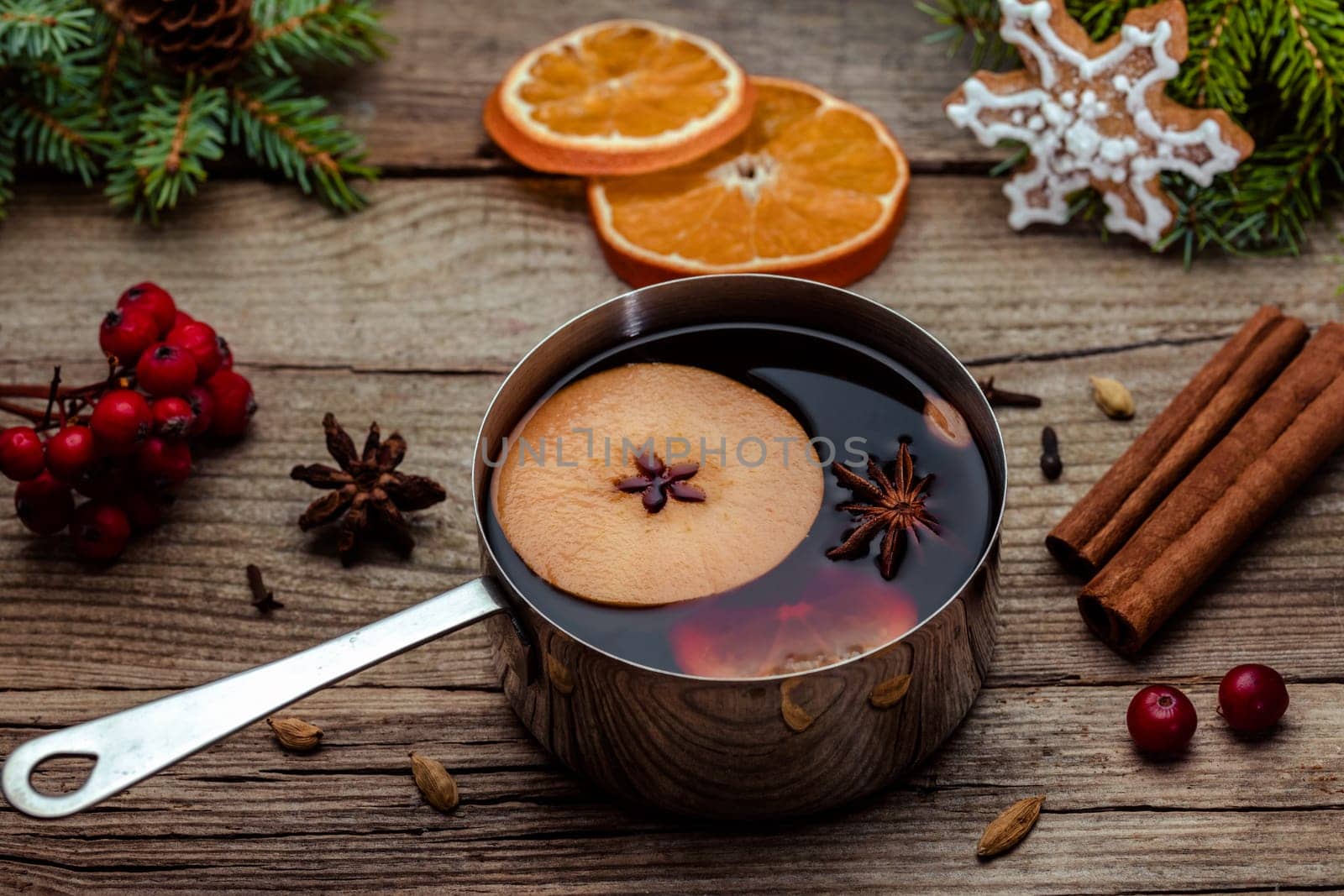 Small stewpot with mulled wine and cinnamon sticks, slice of oranges and apple on wooden table top view. Hot winter drink. Christmas beverage.
