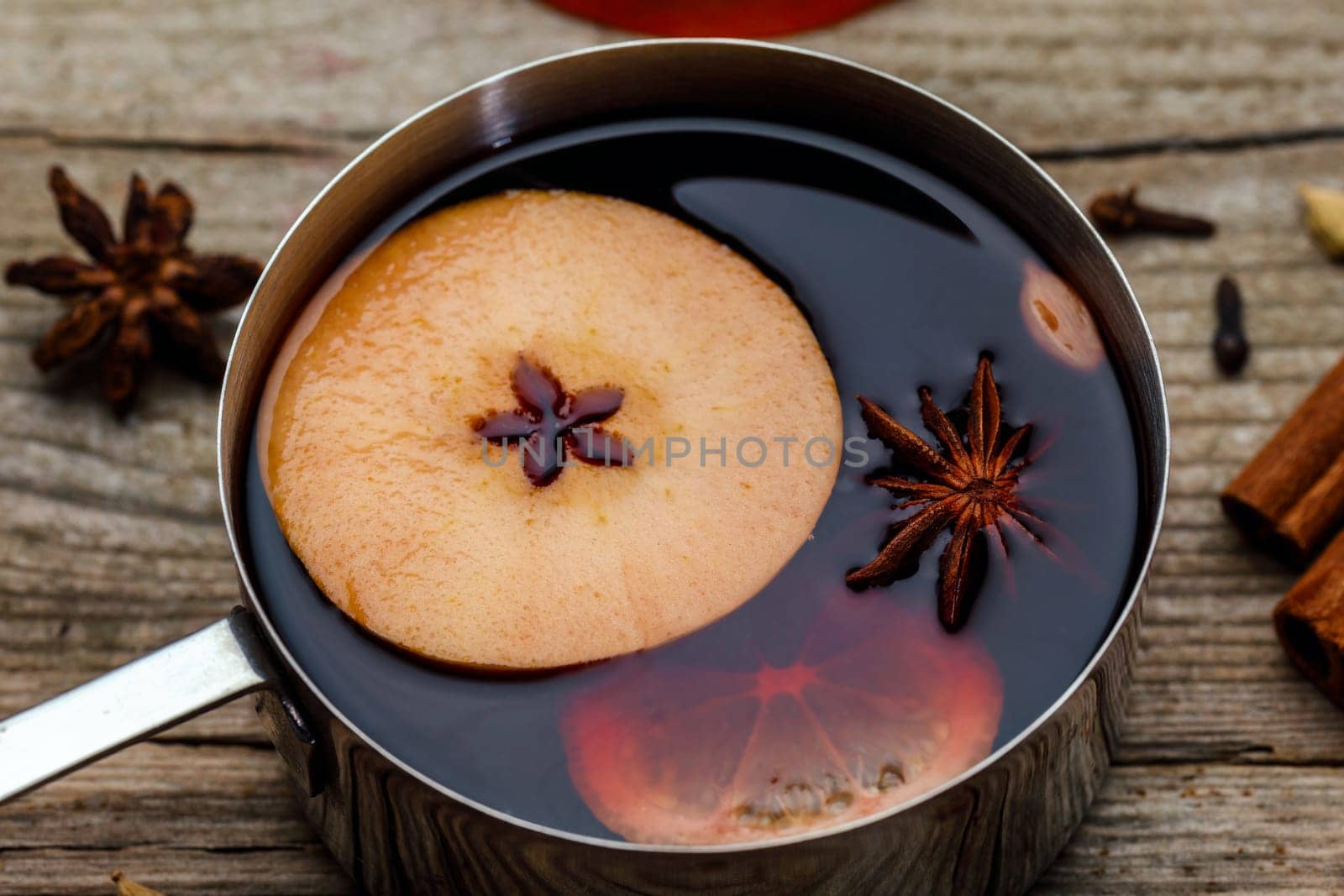 Small stewpot with mulled wine and cinnamon sticks, slice of oranges and apple on wooden table top view. Hot winter drink. Christmas beverage.
