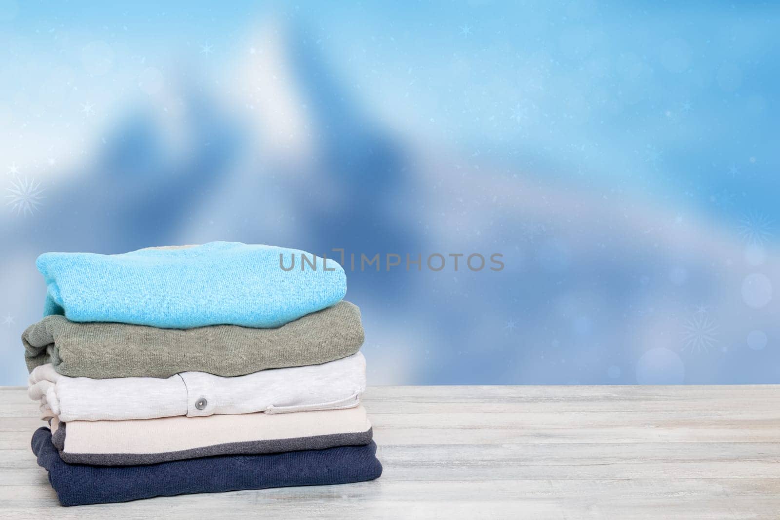 Stack of winter clothes. Pile of colorful knitted cozy warm cashmere sweaters or pullover on wooden table against abstract bright winter background. Space for display product montage. Beautiful backdrop.