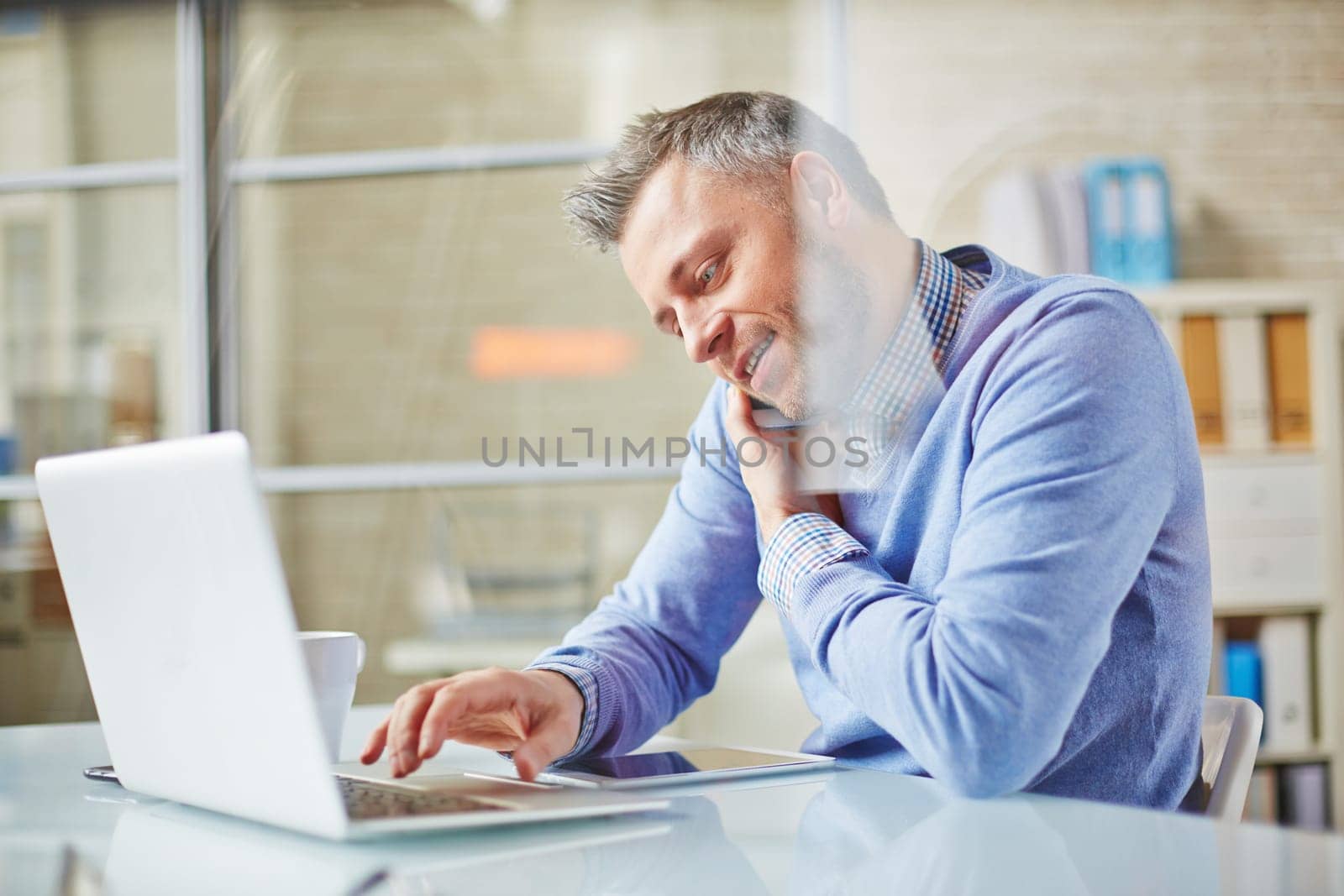 Businessman speaking on cellphone while typing on laptop